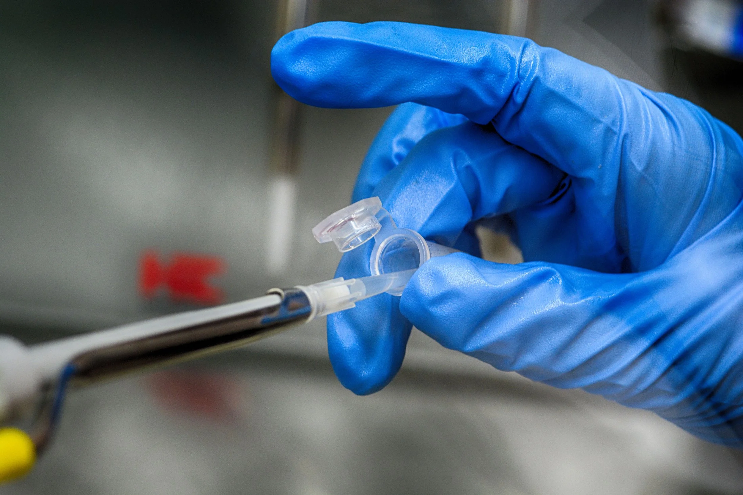 A hand wearing a blue glove holding a syringe with a needle.