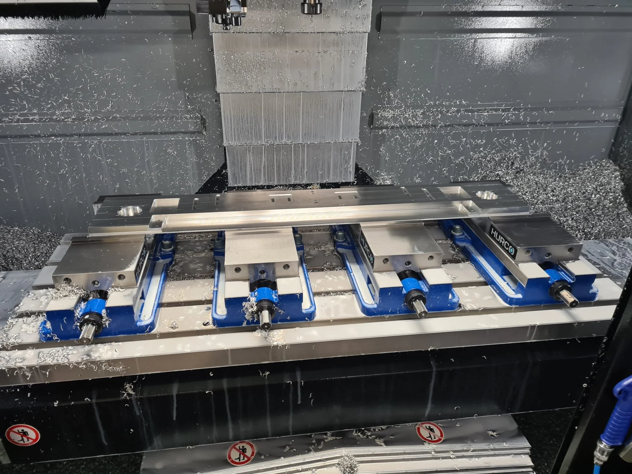 A CNC milling machine in operation cutting a metal workpiece, with metal shavings surrounding the area.