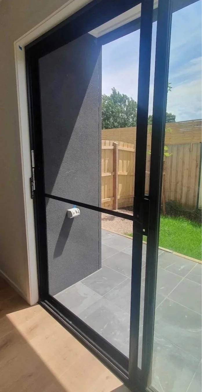 View of a glass sliding patio door opening to an outdoor area with a wooden fence, a small greenhouse, and a grassy lawn.