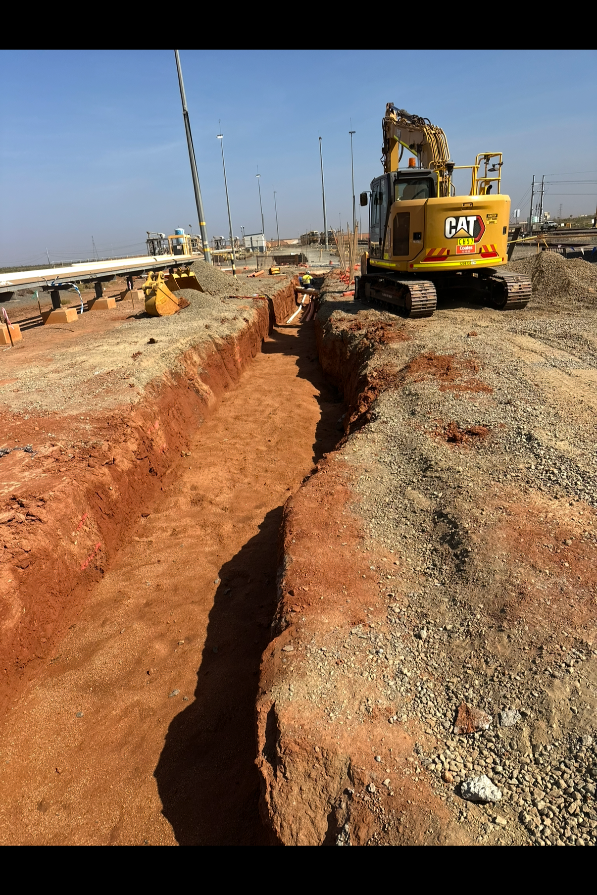 Construction site with excavator digging a trench on a sunny day.
