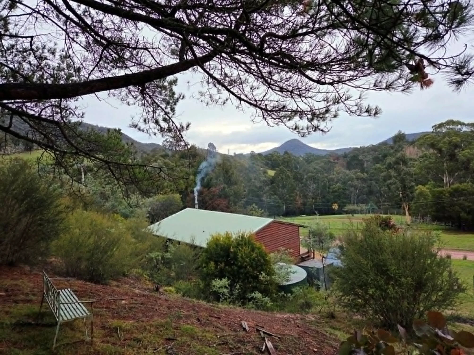 Scenic view of a mountainous landscape with trees, a small building on the hillside, and a cloudy sky.