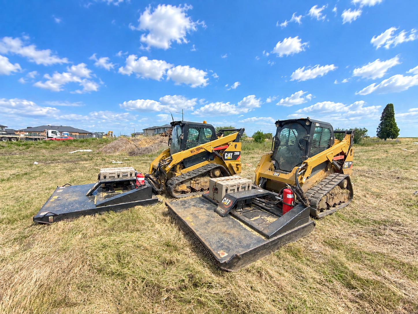 Two yellow CAT compact track loaders parked on grassy field under cloudy sky.