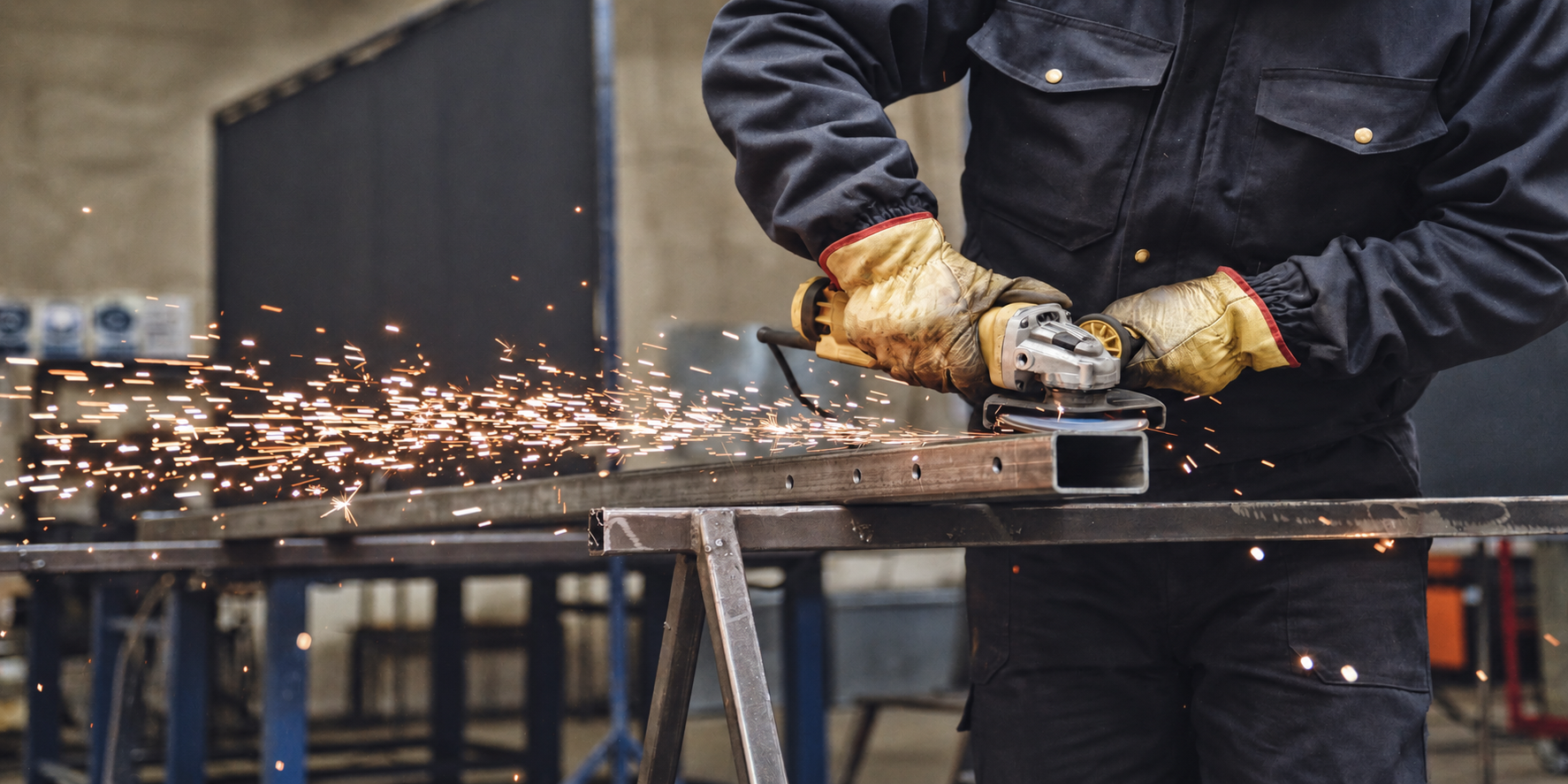 A person wearing work gloves is using an angle grinder to cut or grind a metal piece, with sparks flying from the work surface.