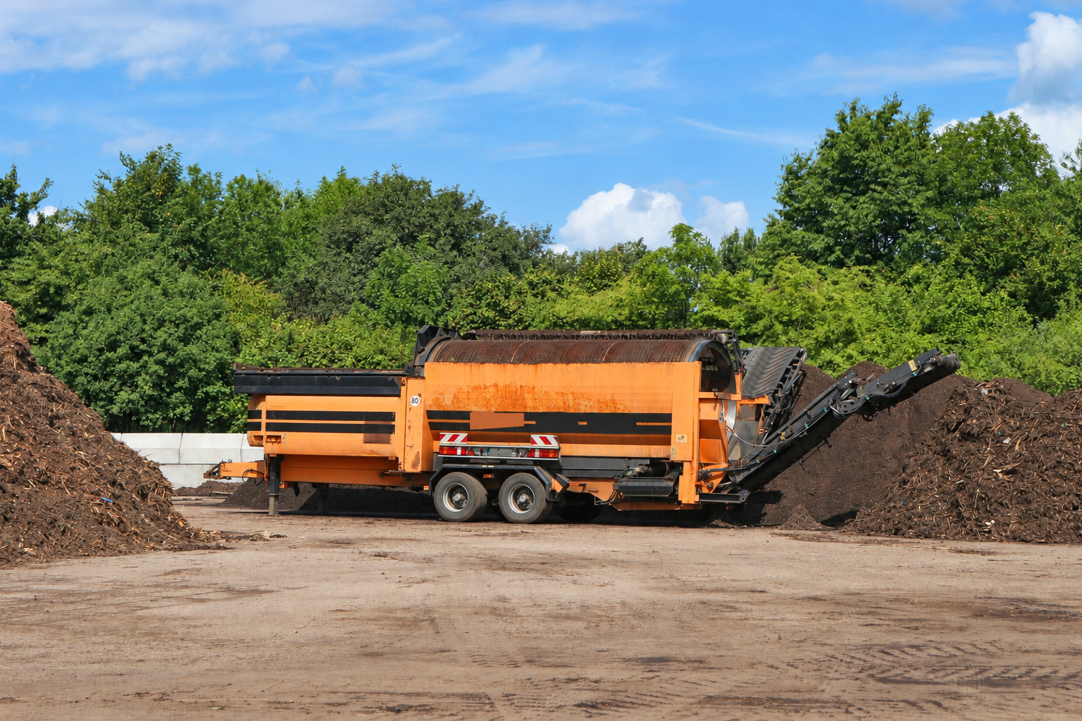 A large pile of mulch with a conveyor belt next to it, likely used for moving or spreading the mulch.