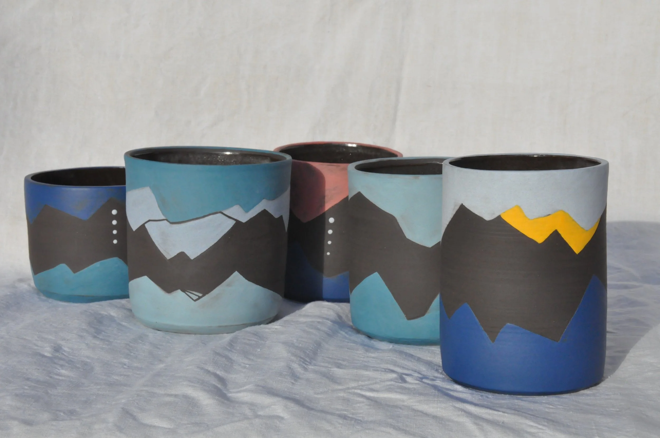 Coupelle en céramique colorée avec motif de montagnes et nuages, exposée sur un fond de neige.