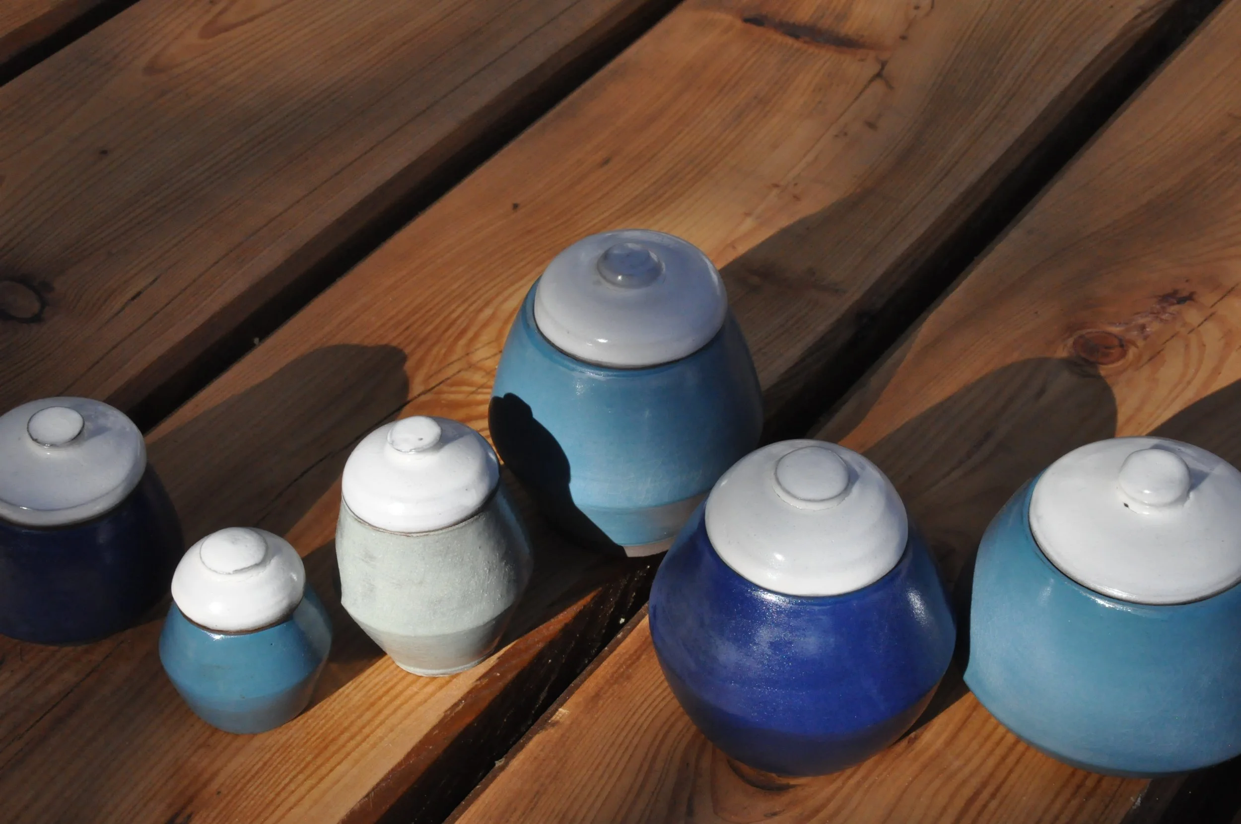 Rangée de petites boîtes colorées en forme de pots de couleur bleue, blanche et gris sur une surface en bois.