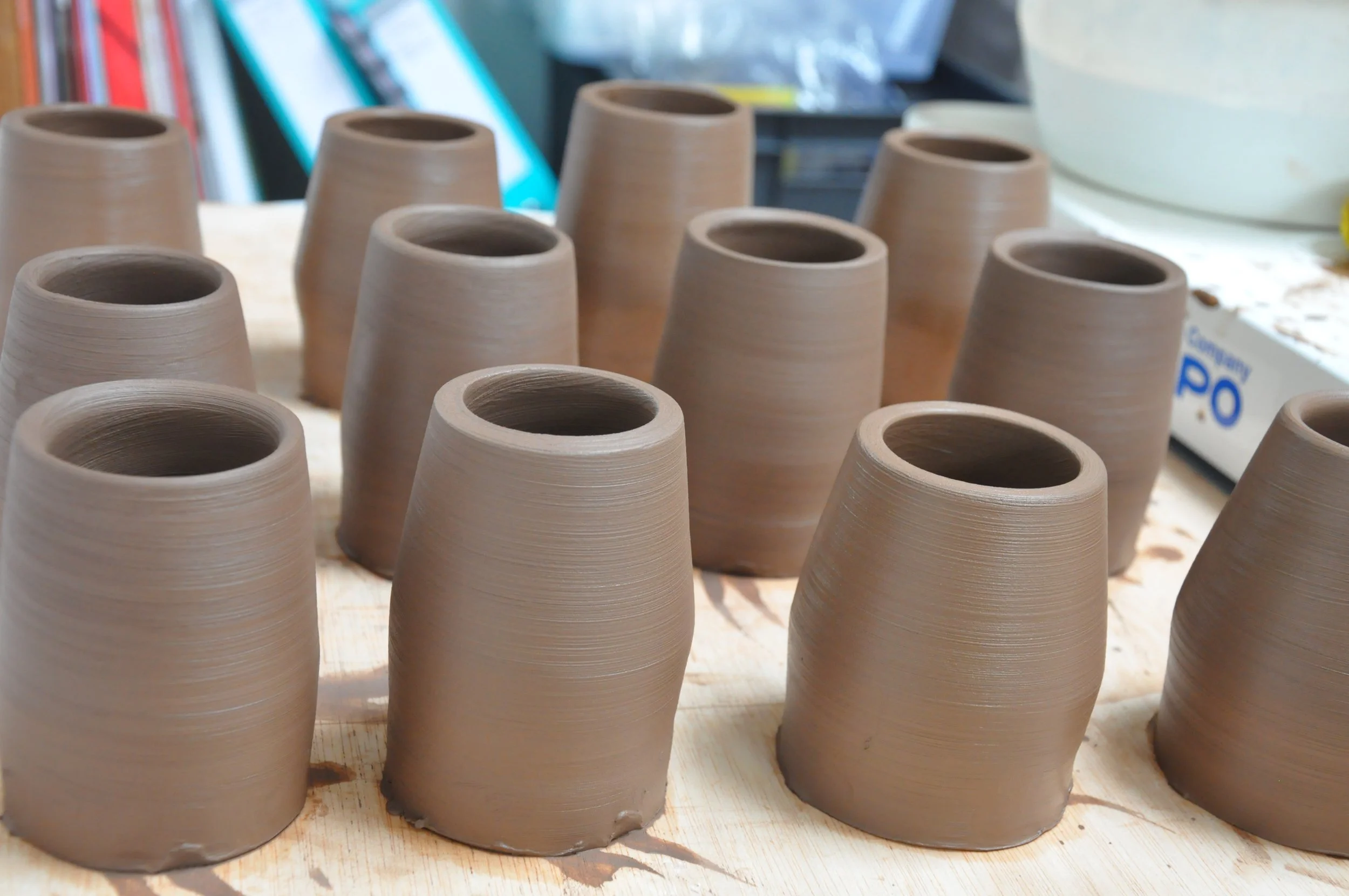 De nombreux cônes en terre cuite non émaillée, disposés sur une table, en cours de fabrication ou de séchage dans un atelier.