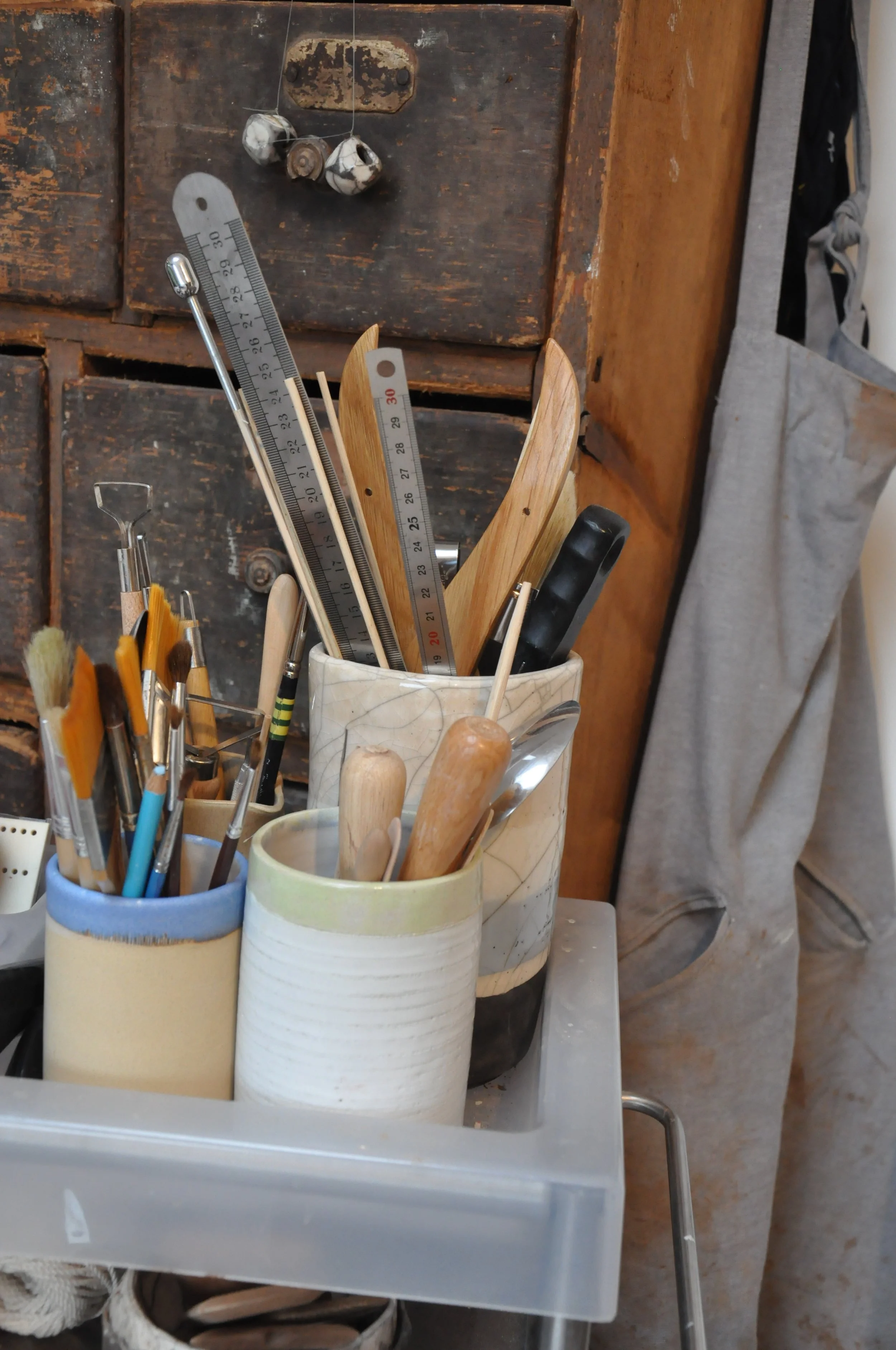 Un ensemble d'outils d'artisanat, notamment des pinceaux, un règle en métal, des outils en bois, dans une pièce de travail rustique avec un vieux meuble en arrière-plan.