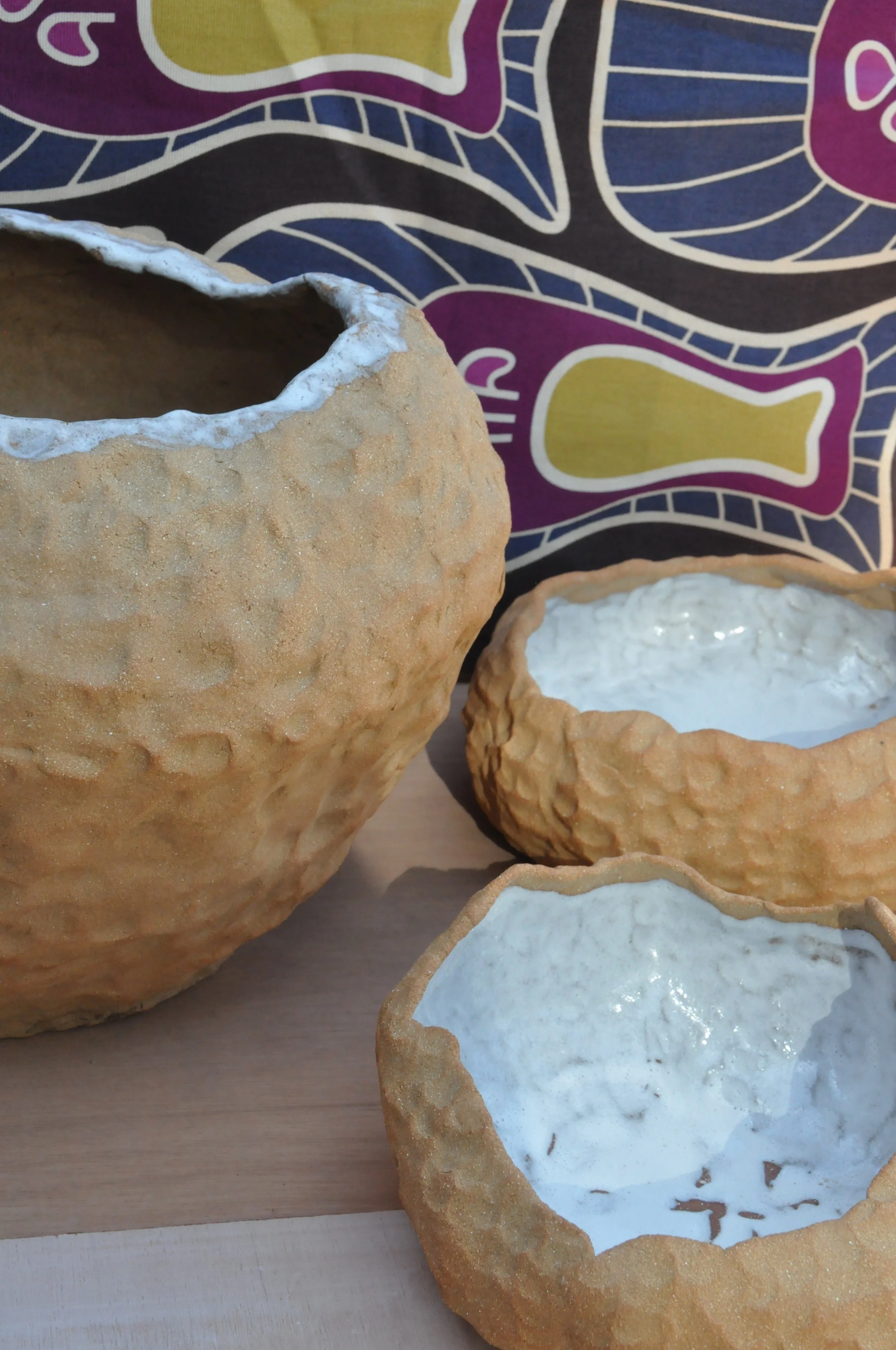 Plats et cache-pots en terre rousse, texturés, avec un intérieur blanc. 