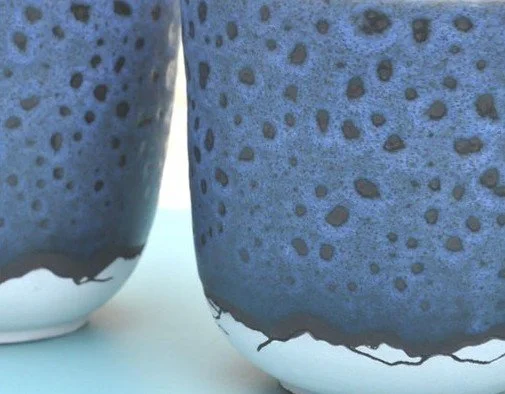 Deux pots en céramique bleus avec des motifs de montagne à la base de la tasse.