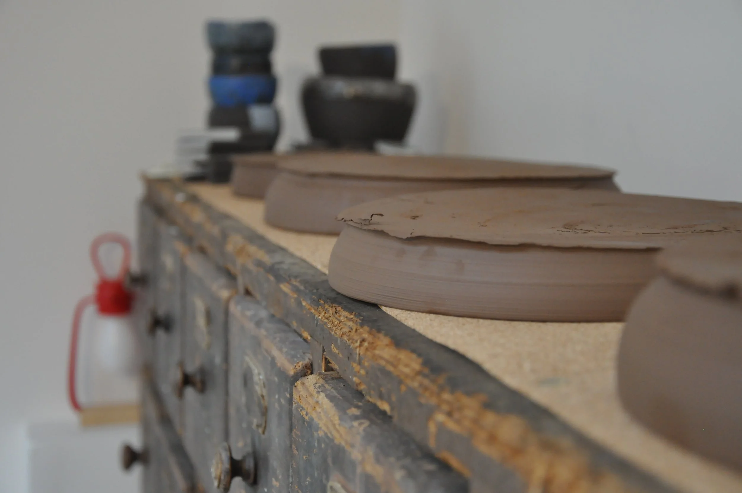 Une planche de bois posée sur une surface de travail usée dans un atelier, avec des pièces en terre crue en train de sécher.