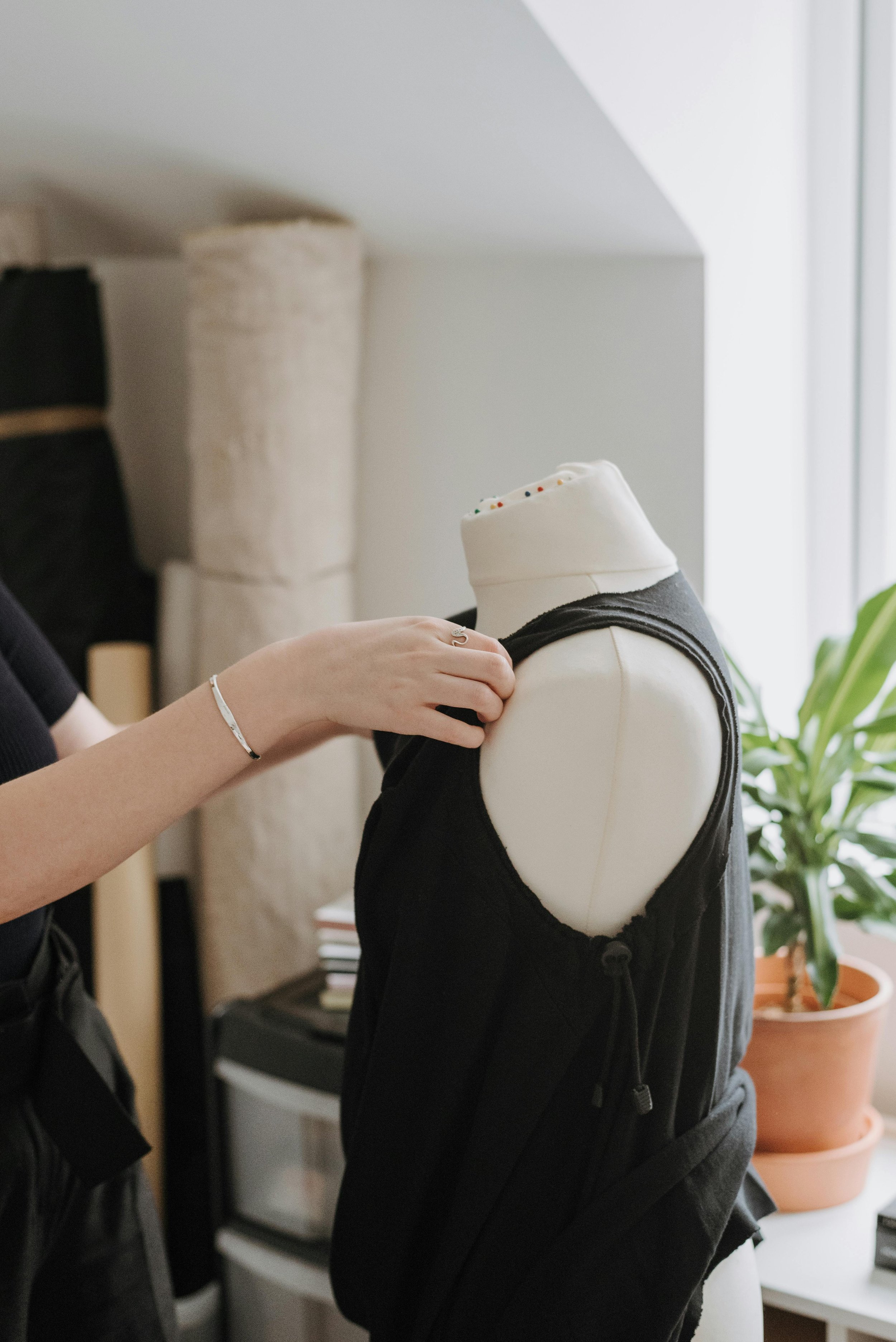 Eine Person passt Kleidung an einem weißen Schneider-Formmodell in einem Raum mit Pflanzen und einem Kamin.