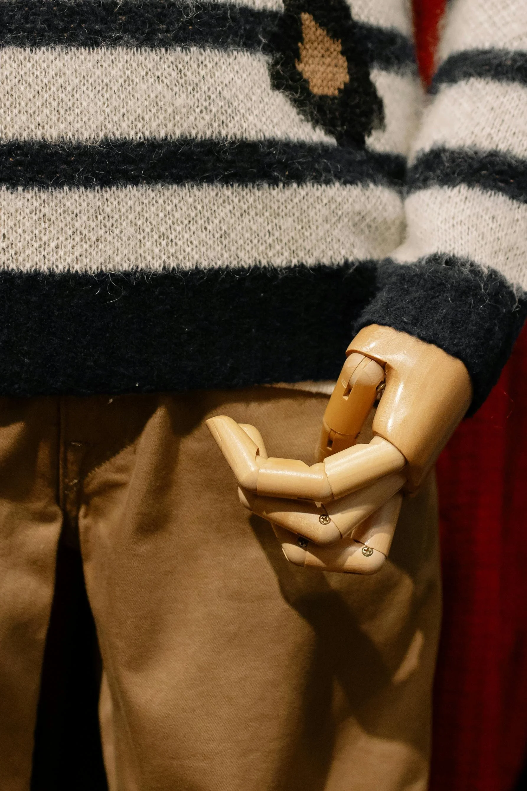 Nahaufnahme eines menschlichen Holzkopfes mit beweglichen Gelenken, der an der Hüfte eines Menschen hängt, der eine braune Hose trägt, im Hintergrund eine gestreifte Wolljacke.