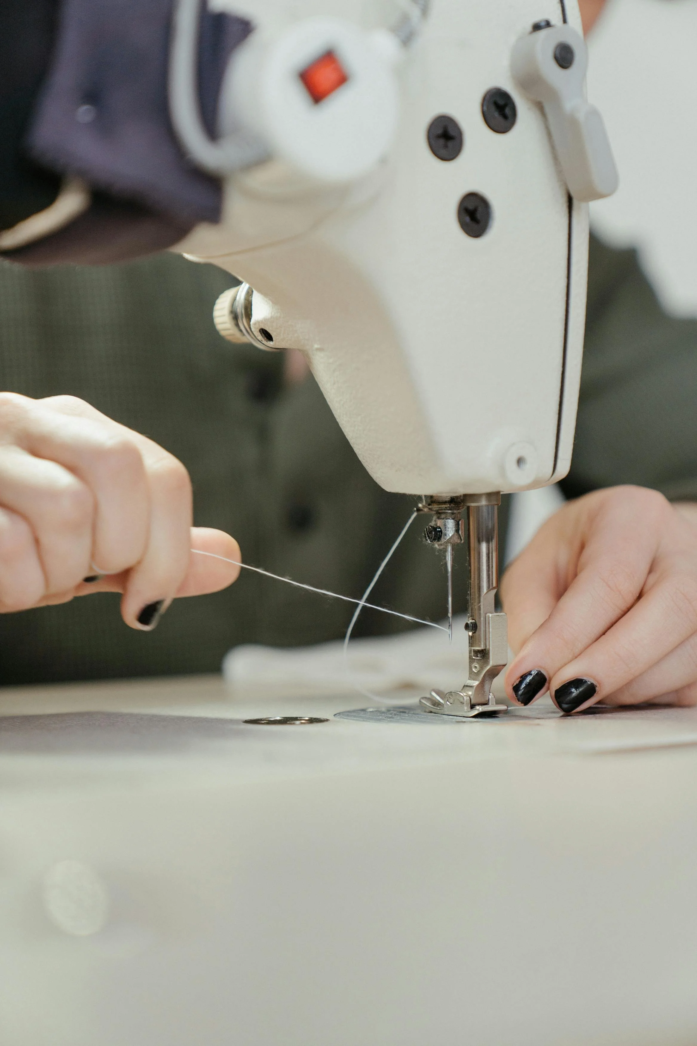 Nahaufnahme einer Person, die eine Nähmaschine benutzt, um Stoff zu nähen, mit Fokus auf die Hände und die Nähmaschine.