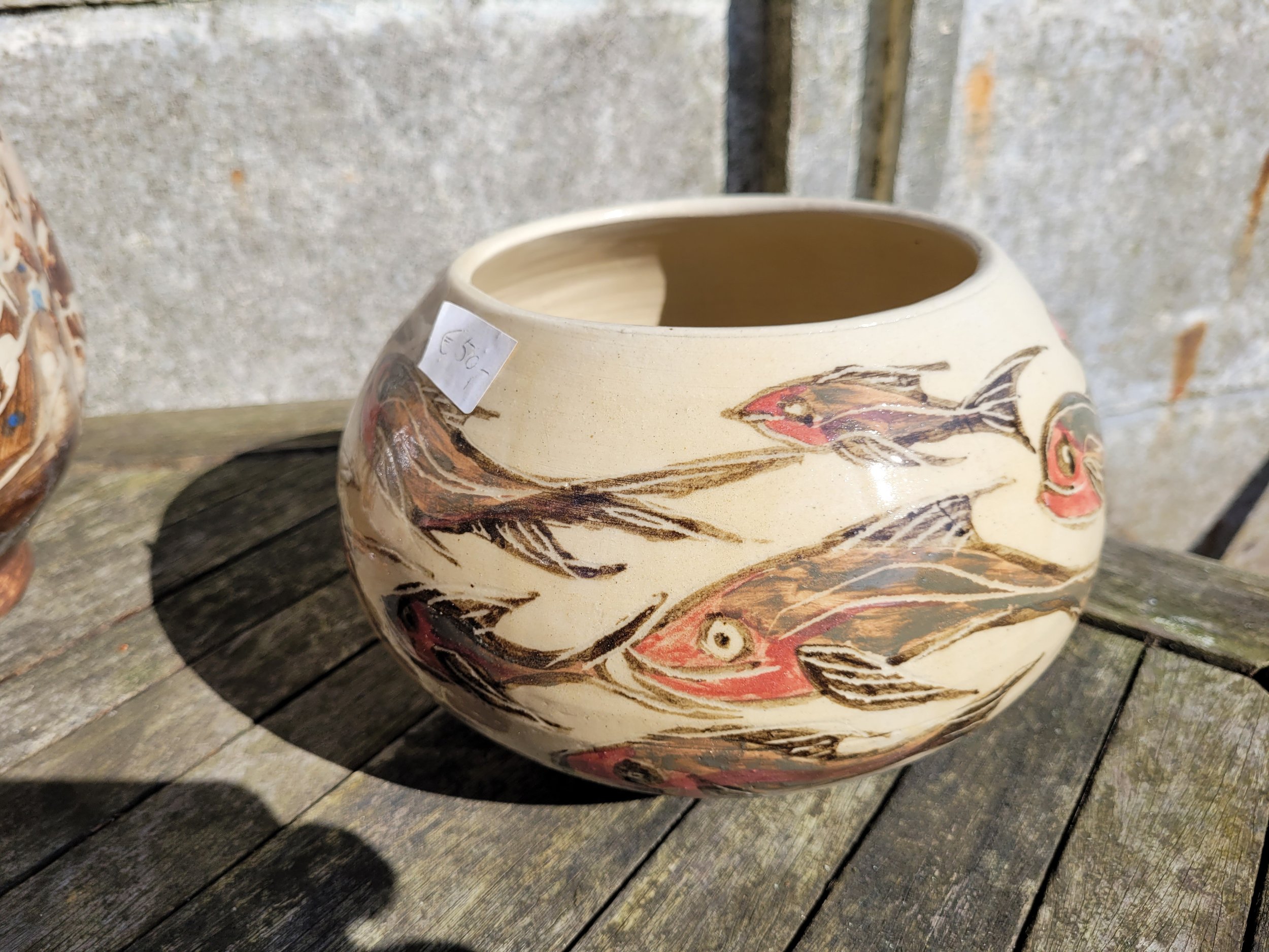 Een keramieken vaas met een kleurrijk, gedetailleerd vogelontwerp, geplaatst op een houten oppervlak tegen een stenen muur.
