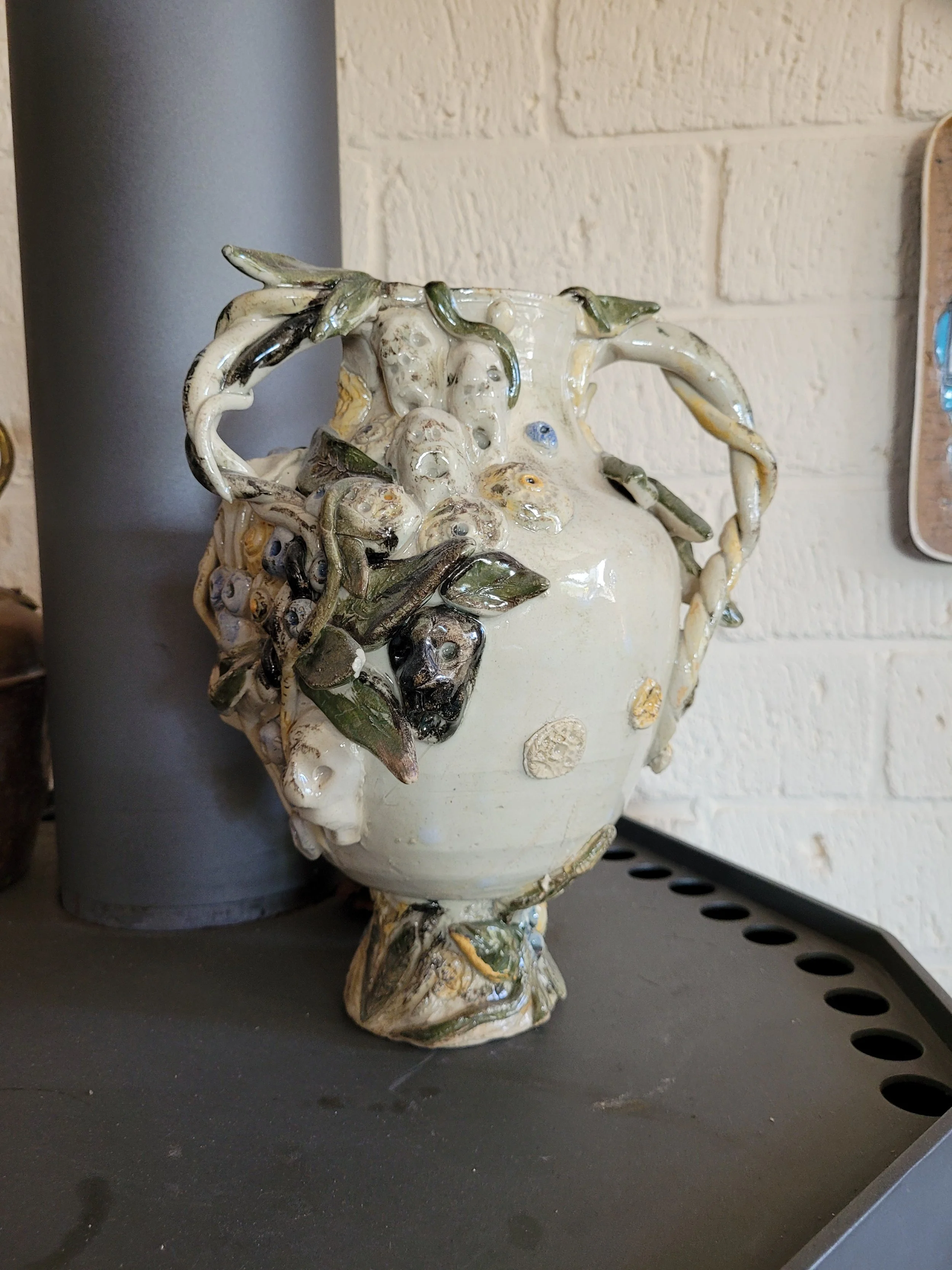 Een sieradenkistje met een bloemmotief, versierd met welving uiteinden en versieringen in groen, wit en blauw, geplaatst op een plank naast een grijze buis en een witte bakwand.