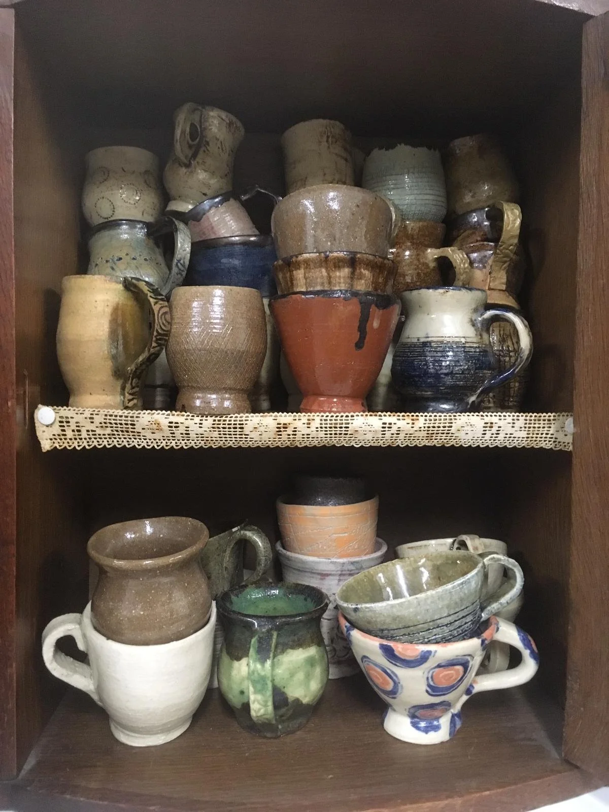 Een houten kast gevuld met diverse keramische bekers en kommen.