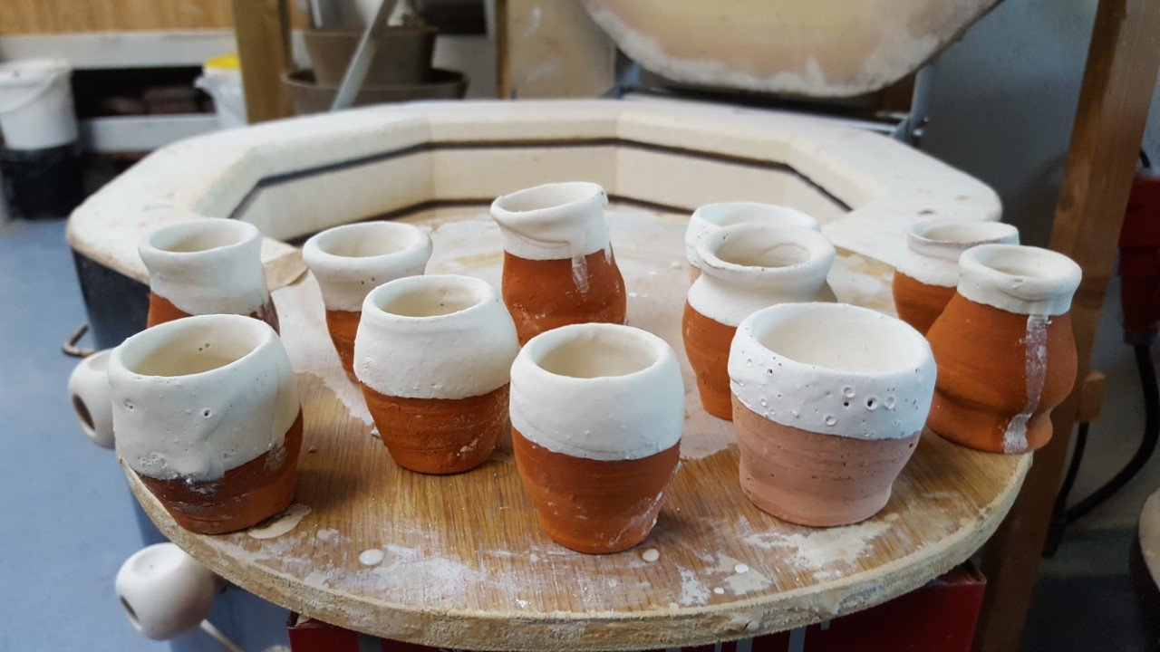 Verschillende keramische potjes en bekers in de maak op een draaischijf in een werkplaats.