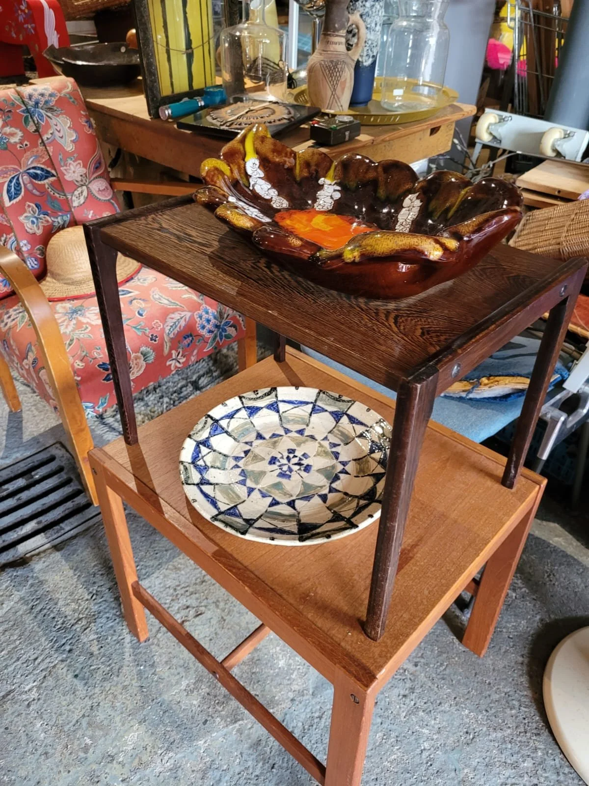 Een houten twee-laagse kar met een decoratieve keramische schaal op de onderste plank en een grote decoratieve kom op de bovenste plank, in een interieur met antieke en vintage decoraties.