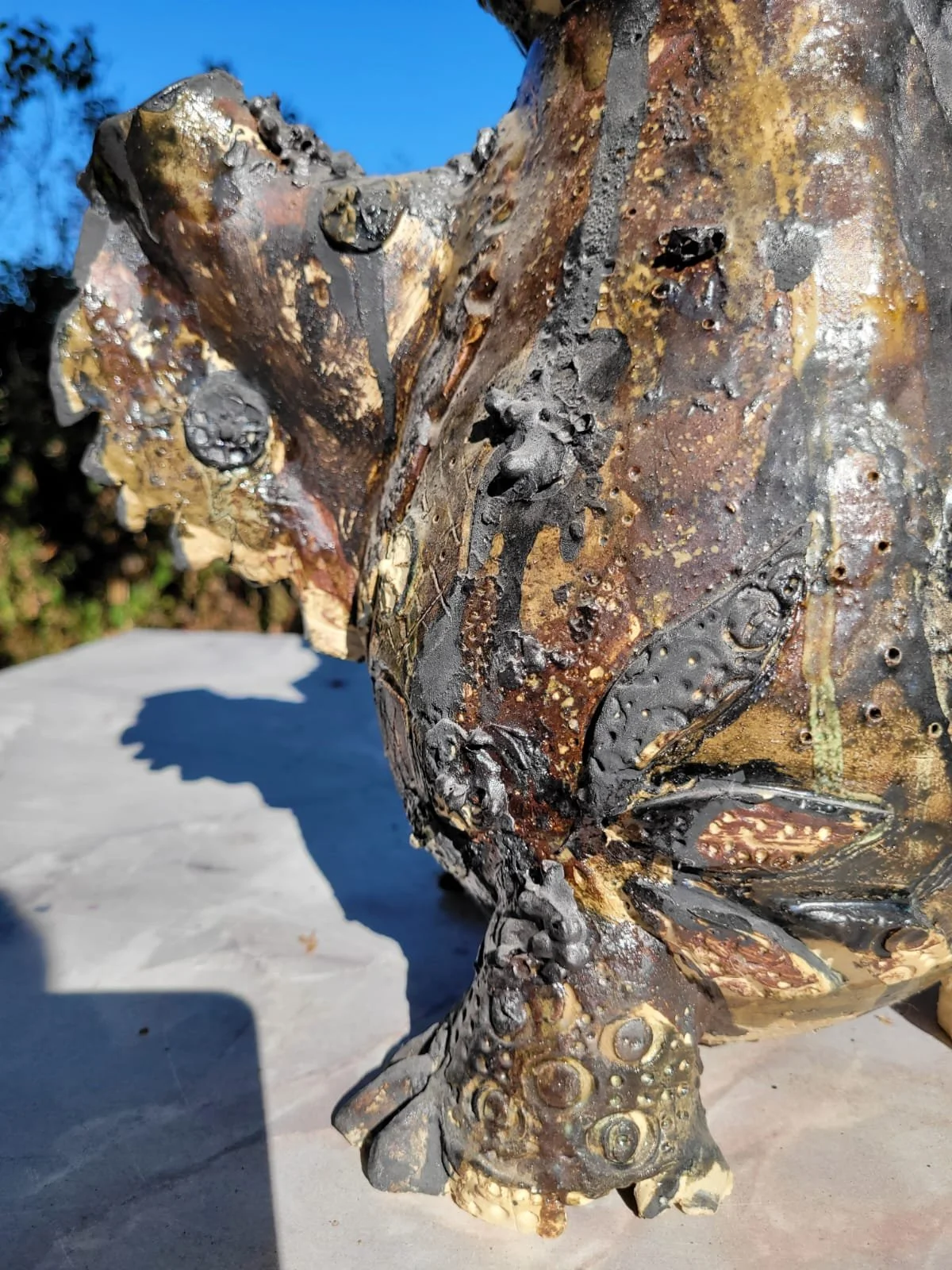 Close-up van een gedetailleerde metalen sculptuur van een hoofd, met textuur en patina, gekleurd in bruin, zwart en oranje tinten.