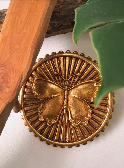 Une décoration murale en forme de papillon en métal doré, entourée de feuilles vertes et d'une structure en bois.