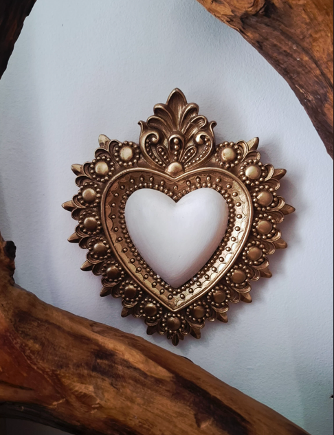 Miroir décoratif en forme de cœur avec une cadre dorée ornée de motifs floraux et de perles, encadré par deux branches ou morceaux de bois.