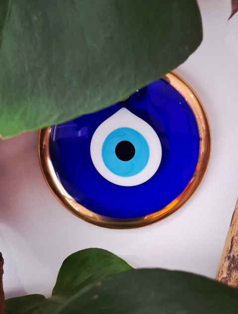 Un pot en céramique bleu avec un œil de décoration en verre au centre, entouré de feuilles vertes.