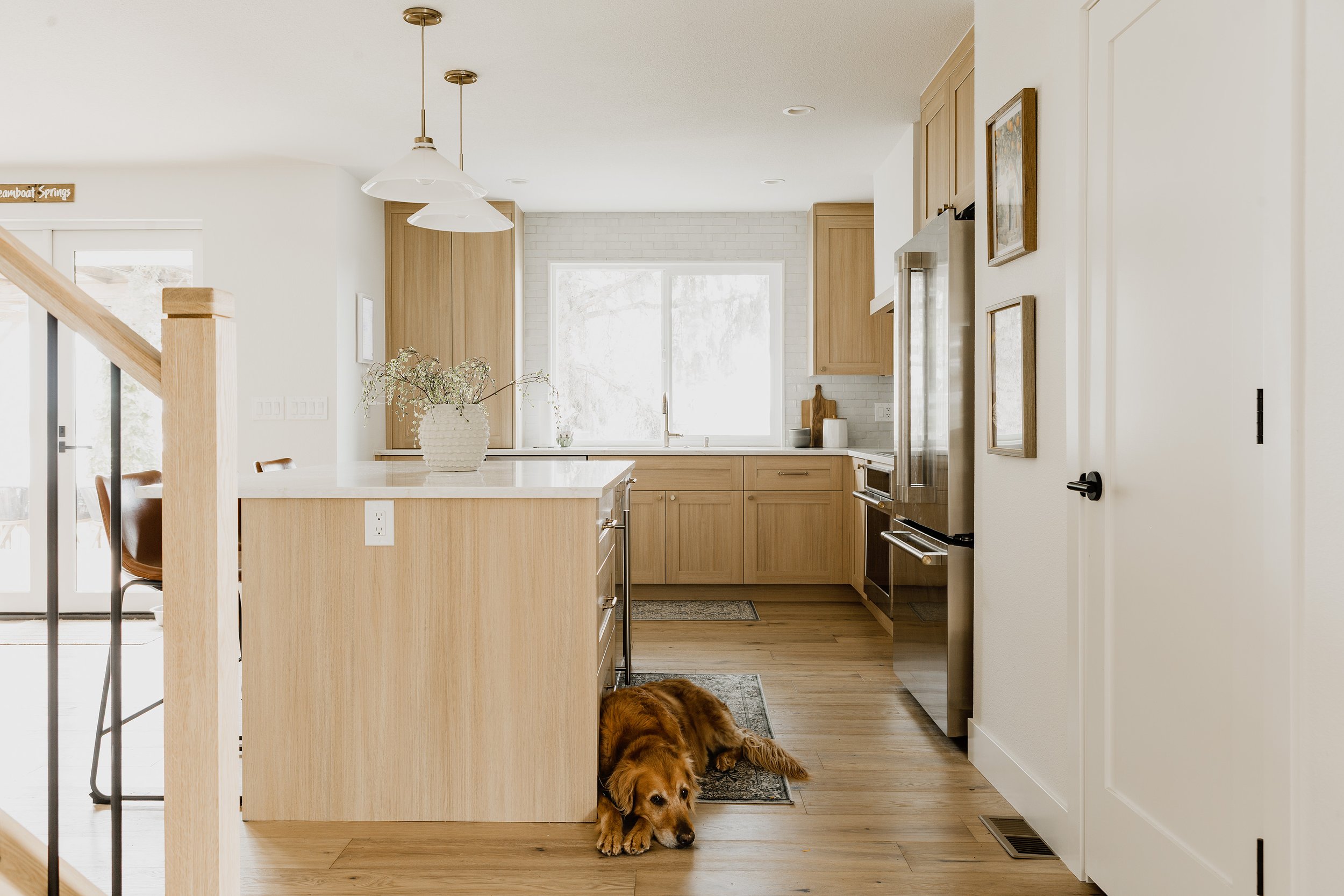 A kitchen with wooden cabinetry, a white brick wall, and a window with snow outside. A dog is lying on the floor near the kitchen island.