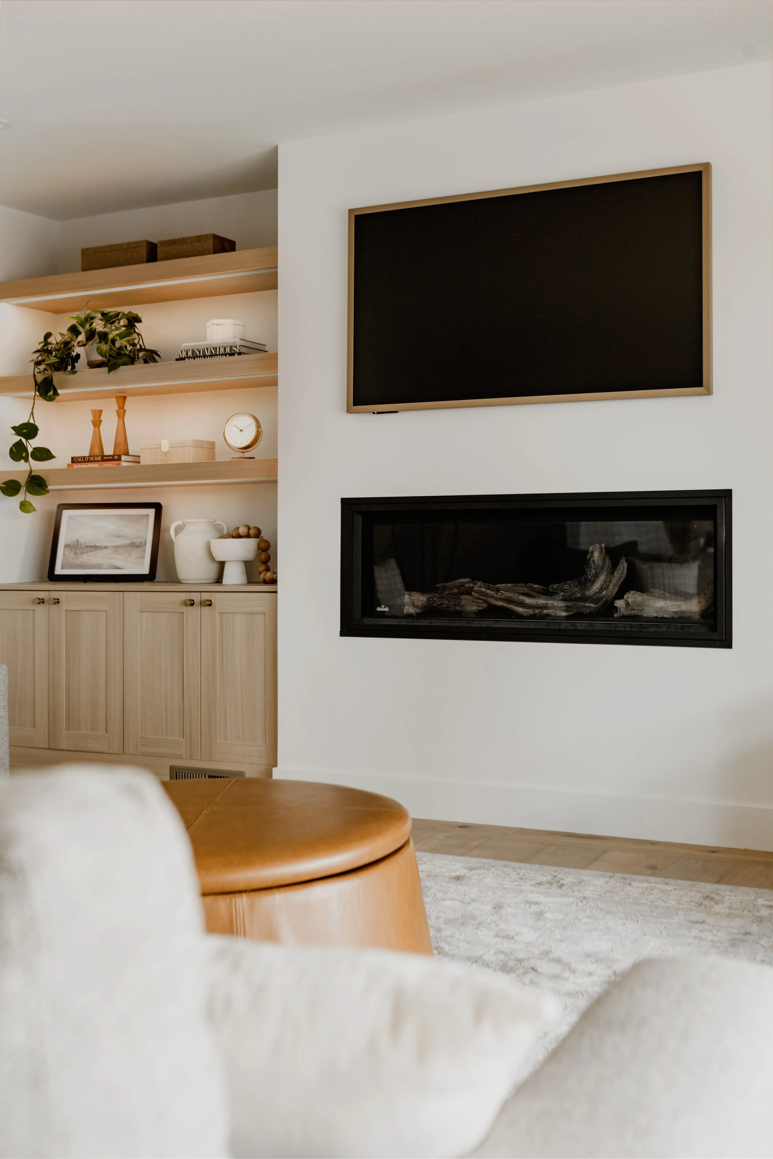 Living room with built-in wooden shelves displaying decor and books, wall-mounted blackboard, and modern fireplace with logs.