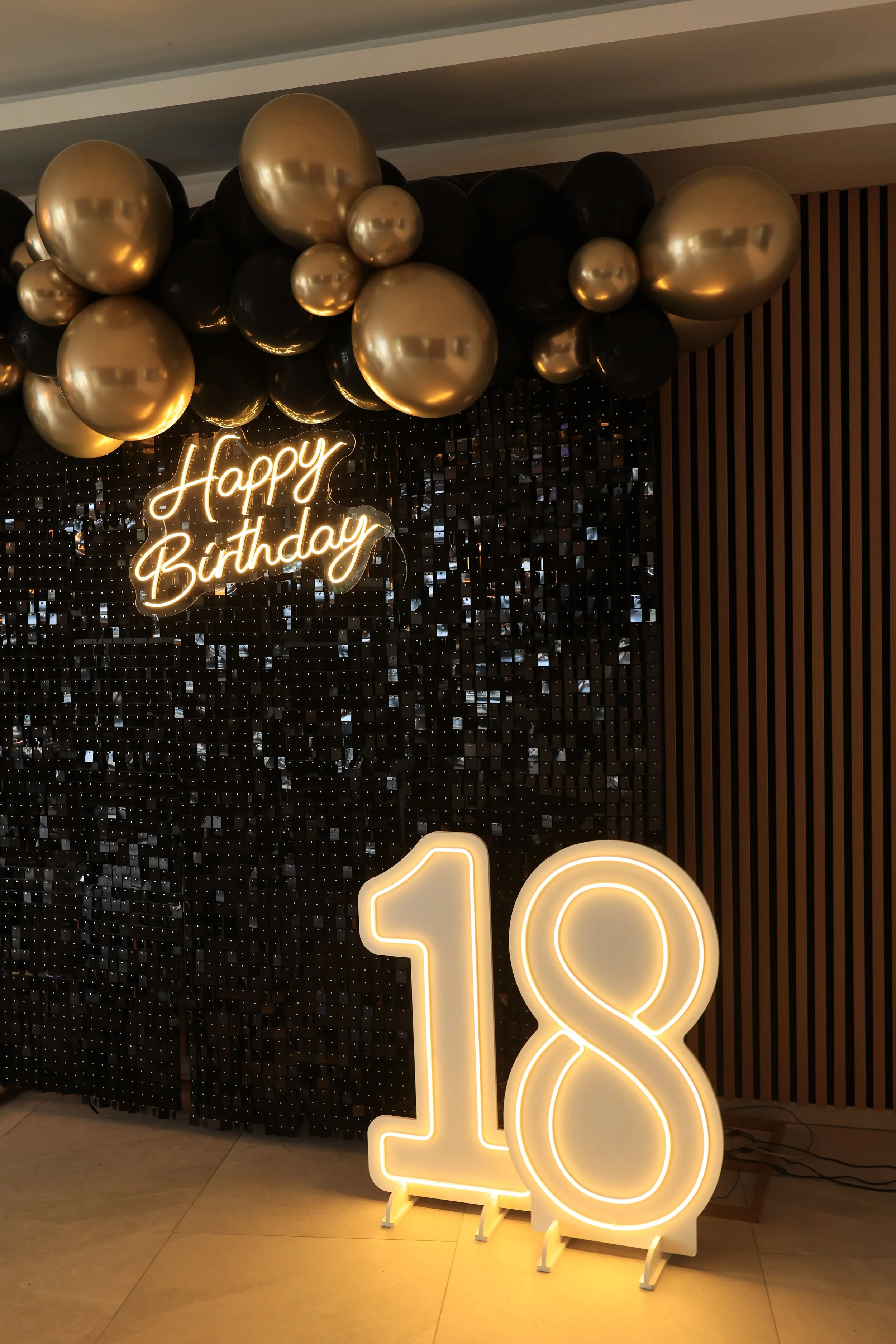 Decorative black and gold balloons arranged above a neon sign reading 'Happy Birthday' and a large illuminated number 10 at a birthday celebration.