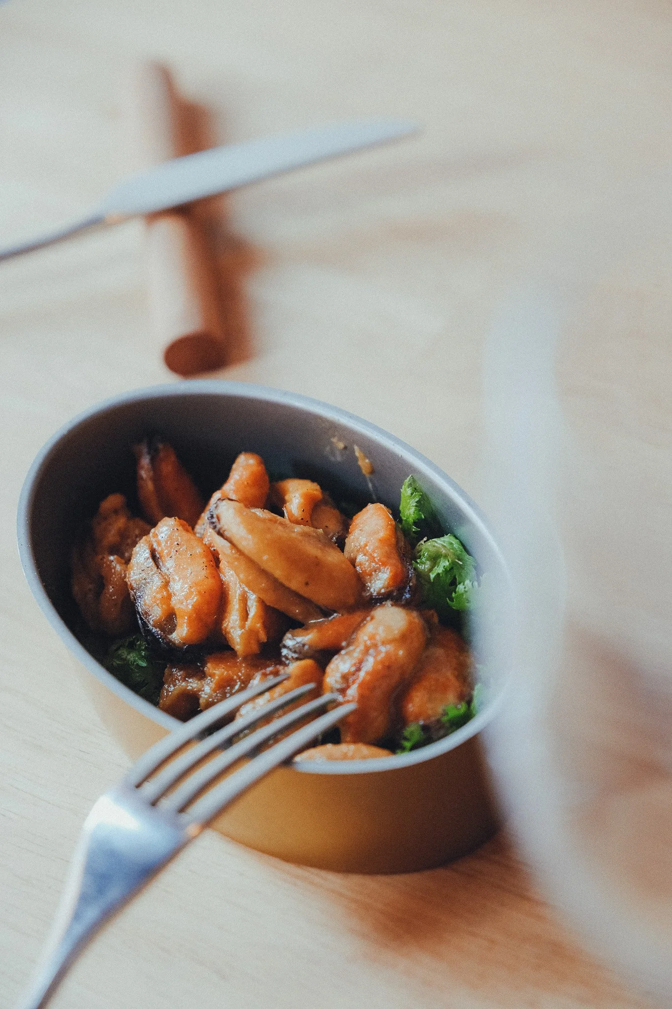 A bowl of cooked chicken pieces garnished with green herbs on a light-colored table with a fork nearby.