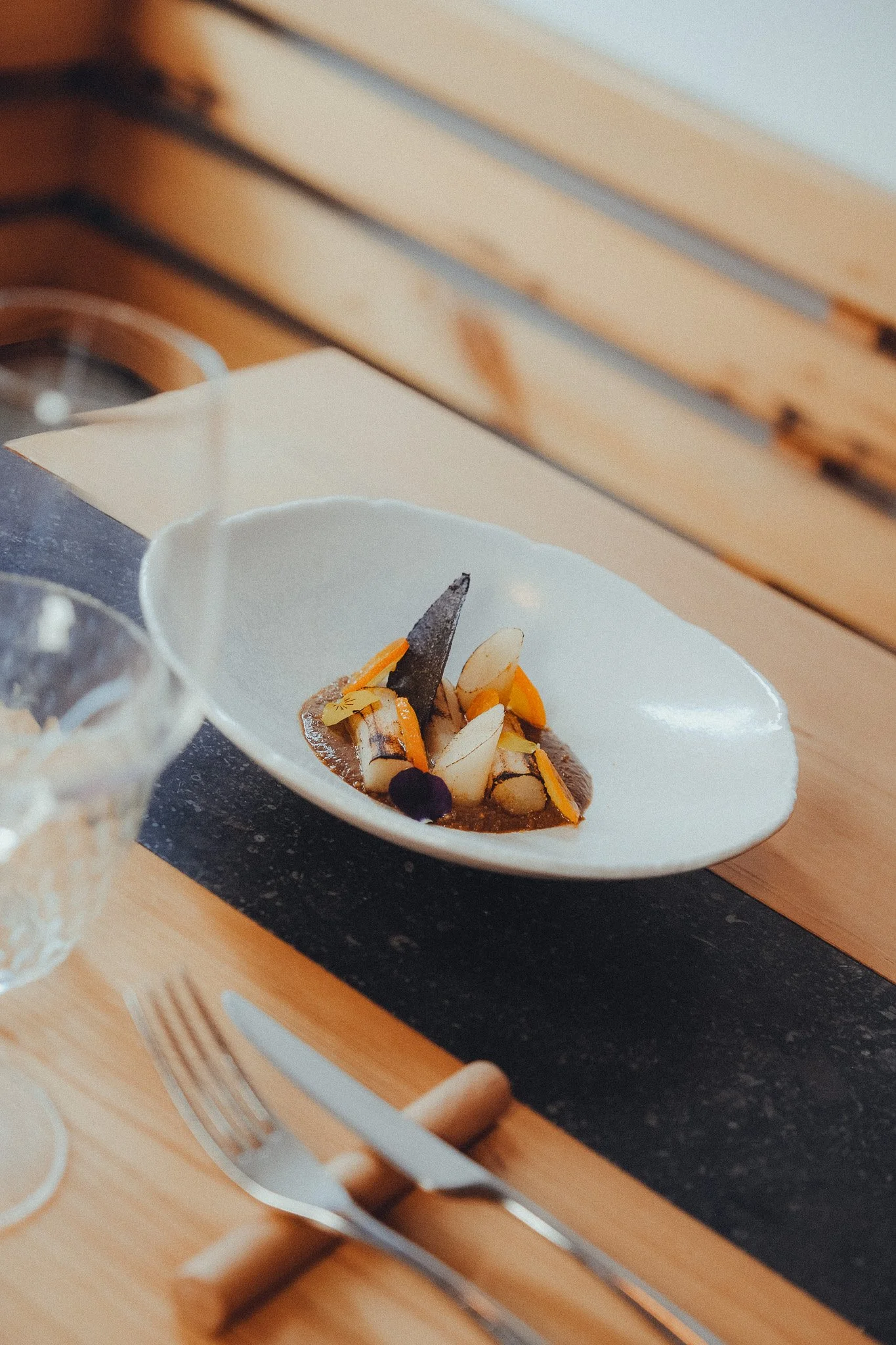 Close-up of a dessert with chocolate, sliced almonds, and fruit on a white plate, placed on a black surface in front of stacked books.