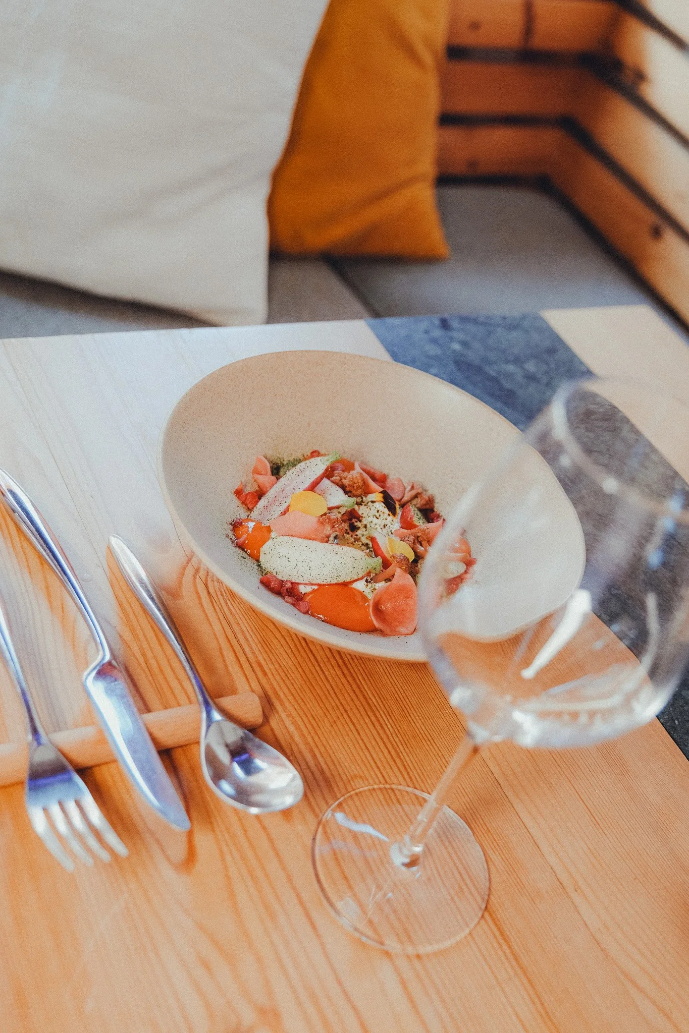 A wine glass with a dessert served in a white bowl, placed on a wooden table with silverware nearby.