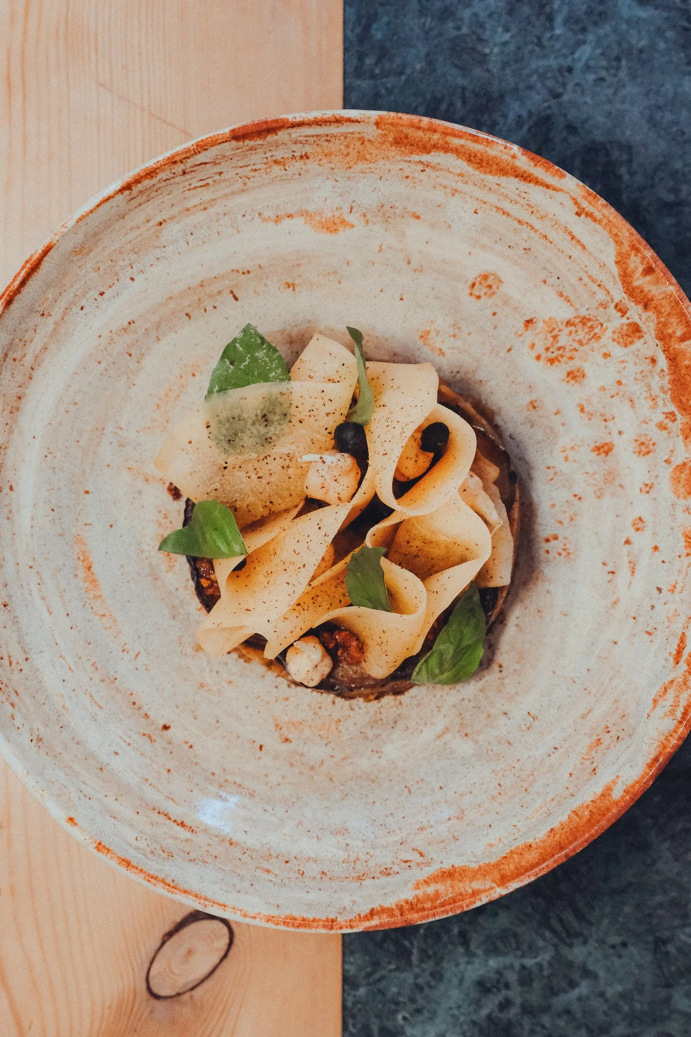 Close-up of a plated dish with pasta, garnished with fresh basil leaves and black pepper, in a rustic ceramic bowl.