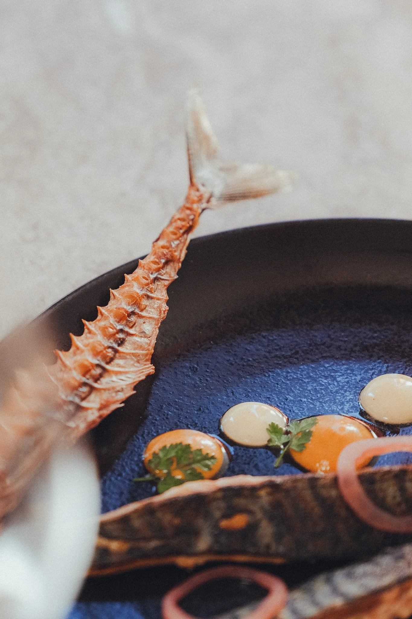 Close-up of a seafood dish featuring a lobster claw, cherry tomatoes, and herbs on a dark plate with a textured surface.