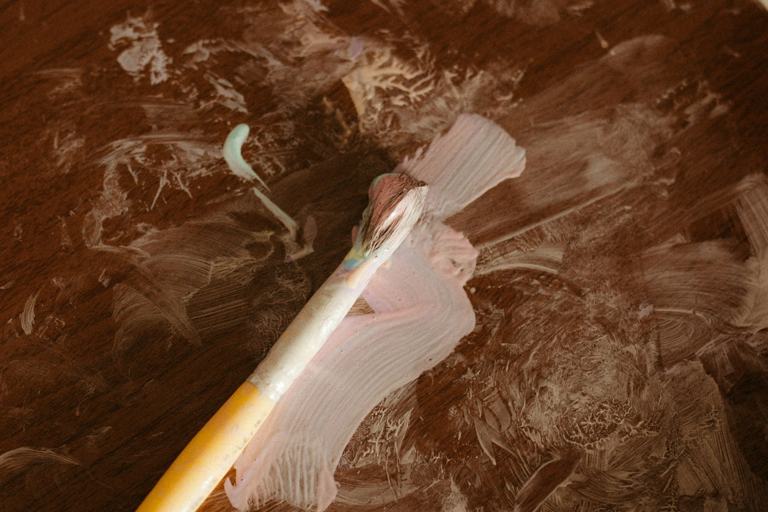 Paintbrushes with pink paint on a wood surface.