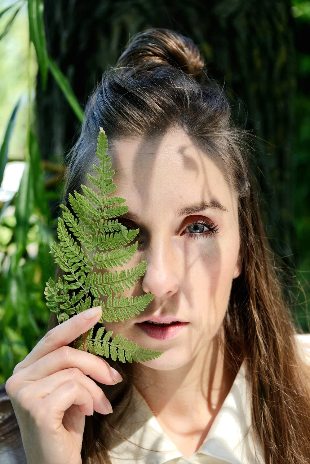 Anastasia Kovaleva holds a green fern leaf in front of her face, covering her left eye