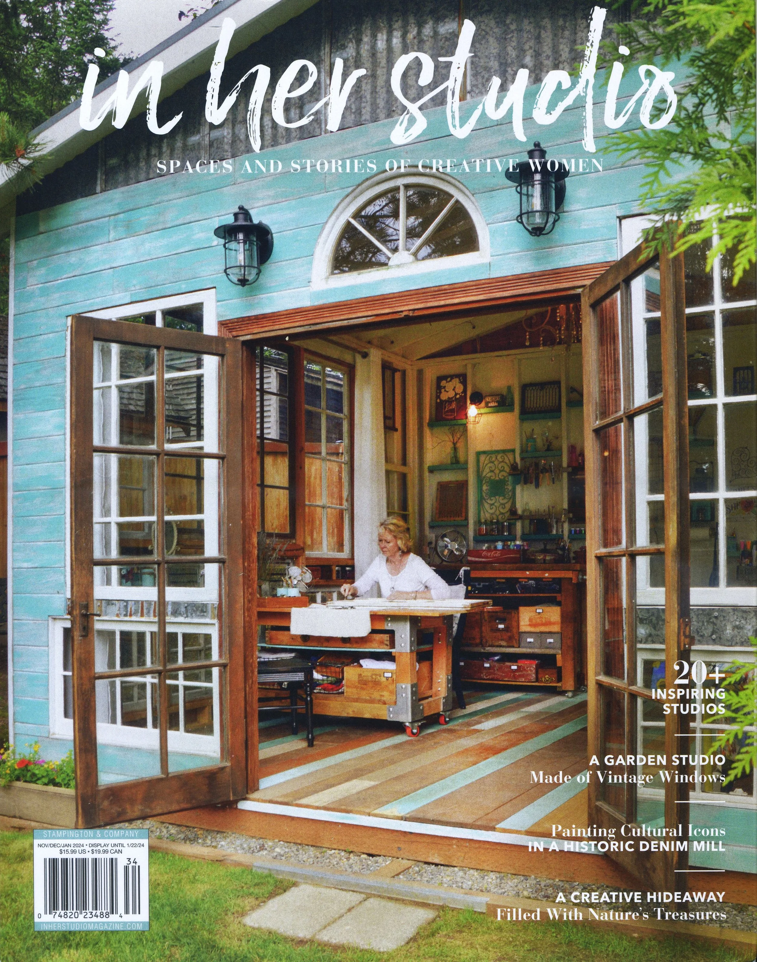 Cover of magazine featuring a cozy garden studio made from vintage windows with open doors, inside a person is working at a desk surrounded by artwork and plants.