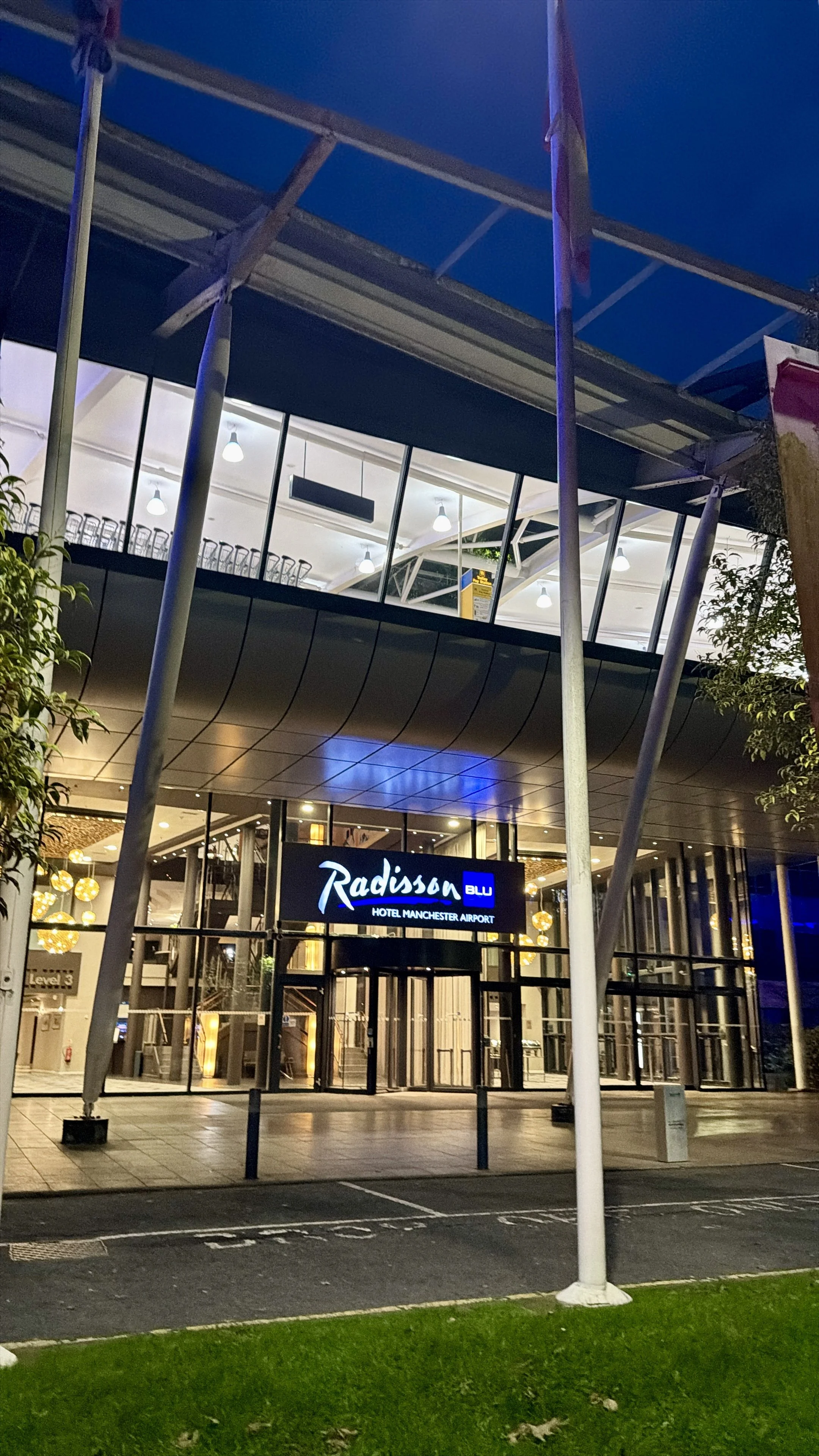 Nighttime exterior of the Radisson Blu Hotel Manchester Airport entrance, illuminated behind a covered drop-off area.