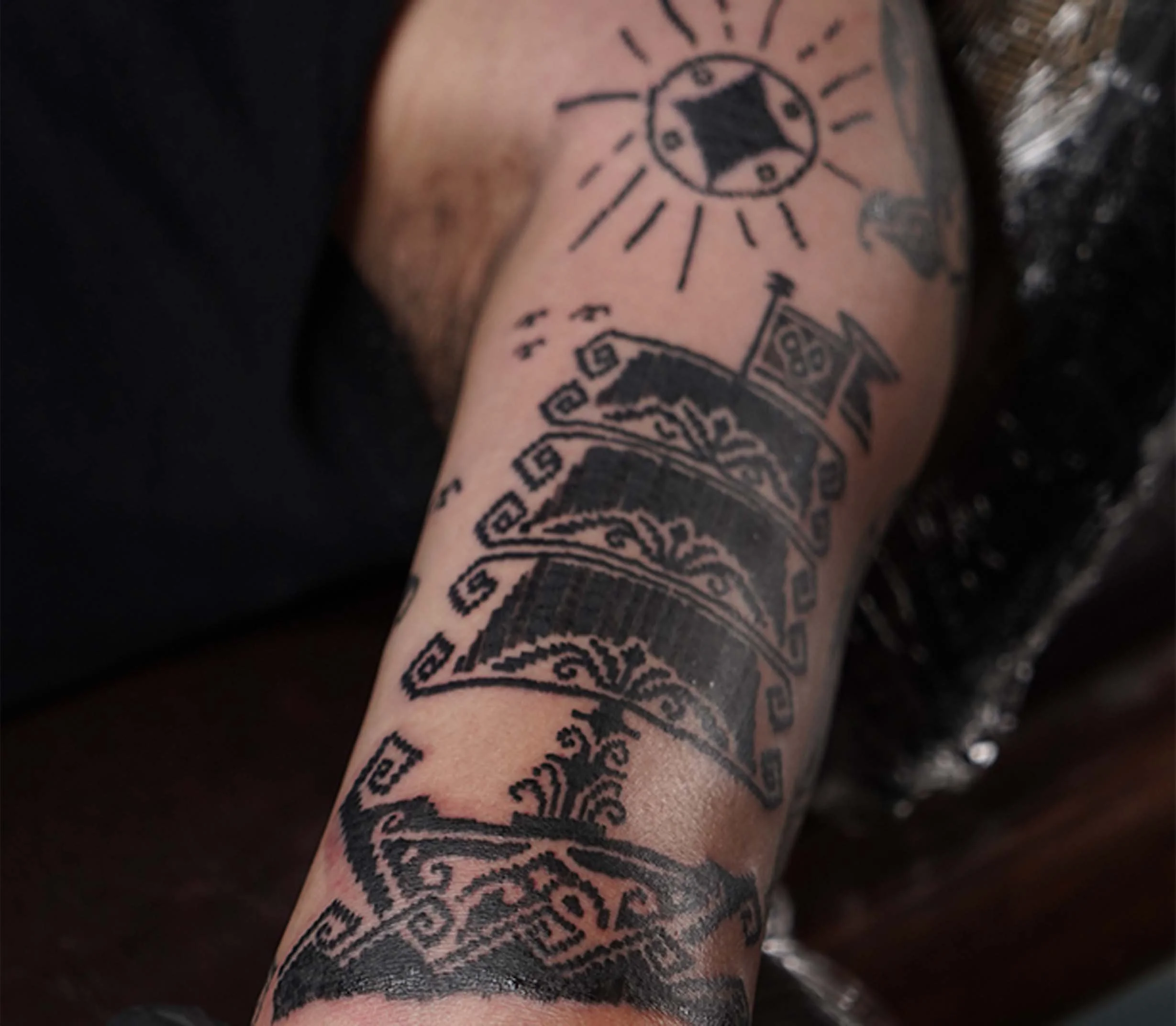 Tattoo of a sun with a face and rays, a moon, and a patterned band on a person's arm.