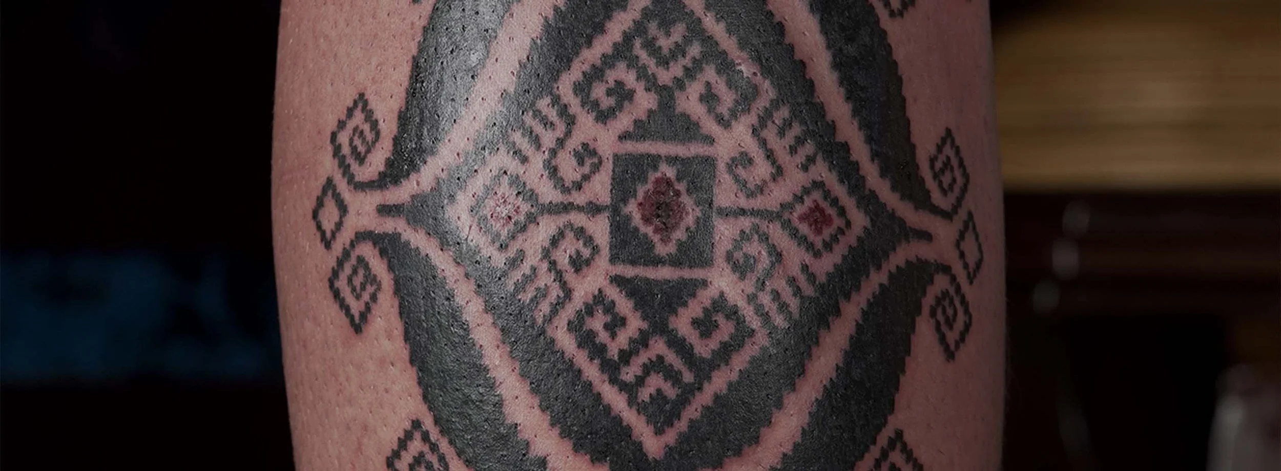Close-up of a geometric black and red tattoo on skin featuring diamonds, squares, and intricate patterns.