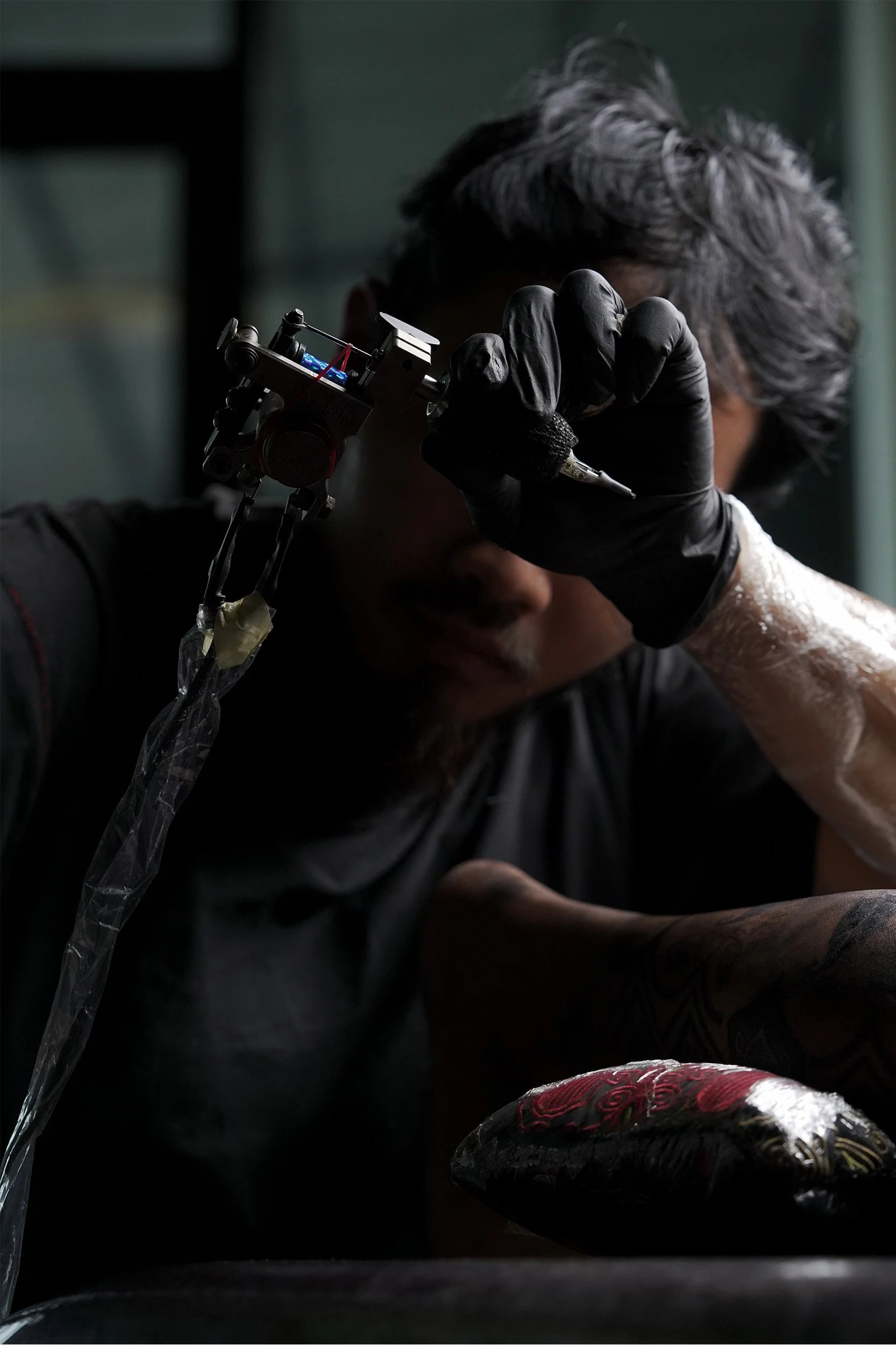 Tattoo artist with black gloves tattooing a person's arm, focusing on the tattooing process.