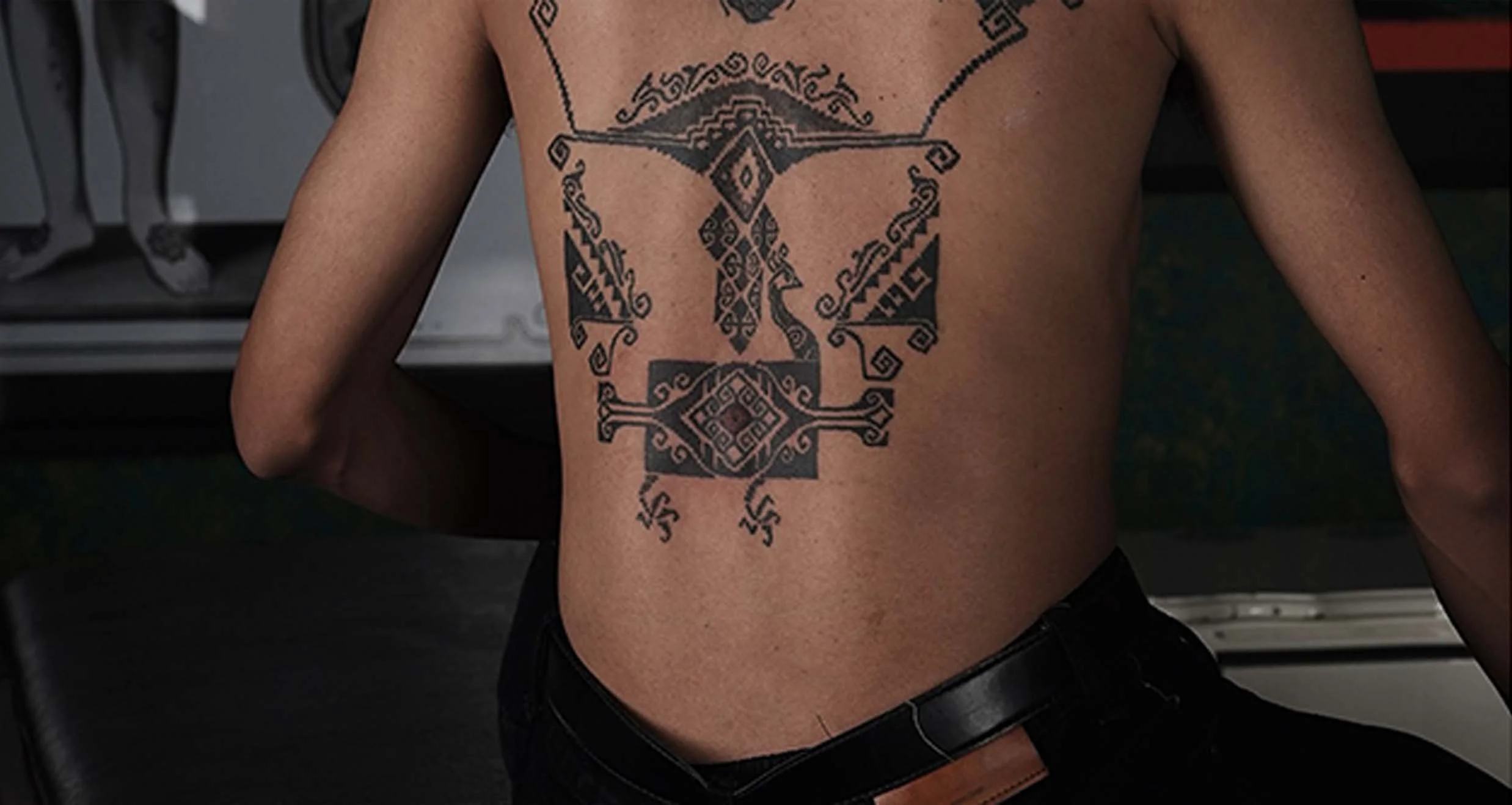A person's back with a large black tattoo featuring intricate geometric and tribal patterns.