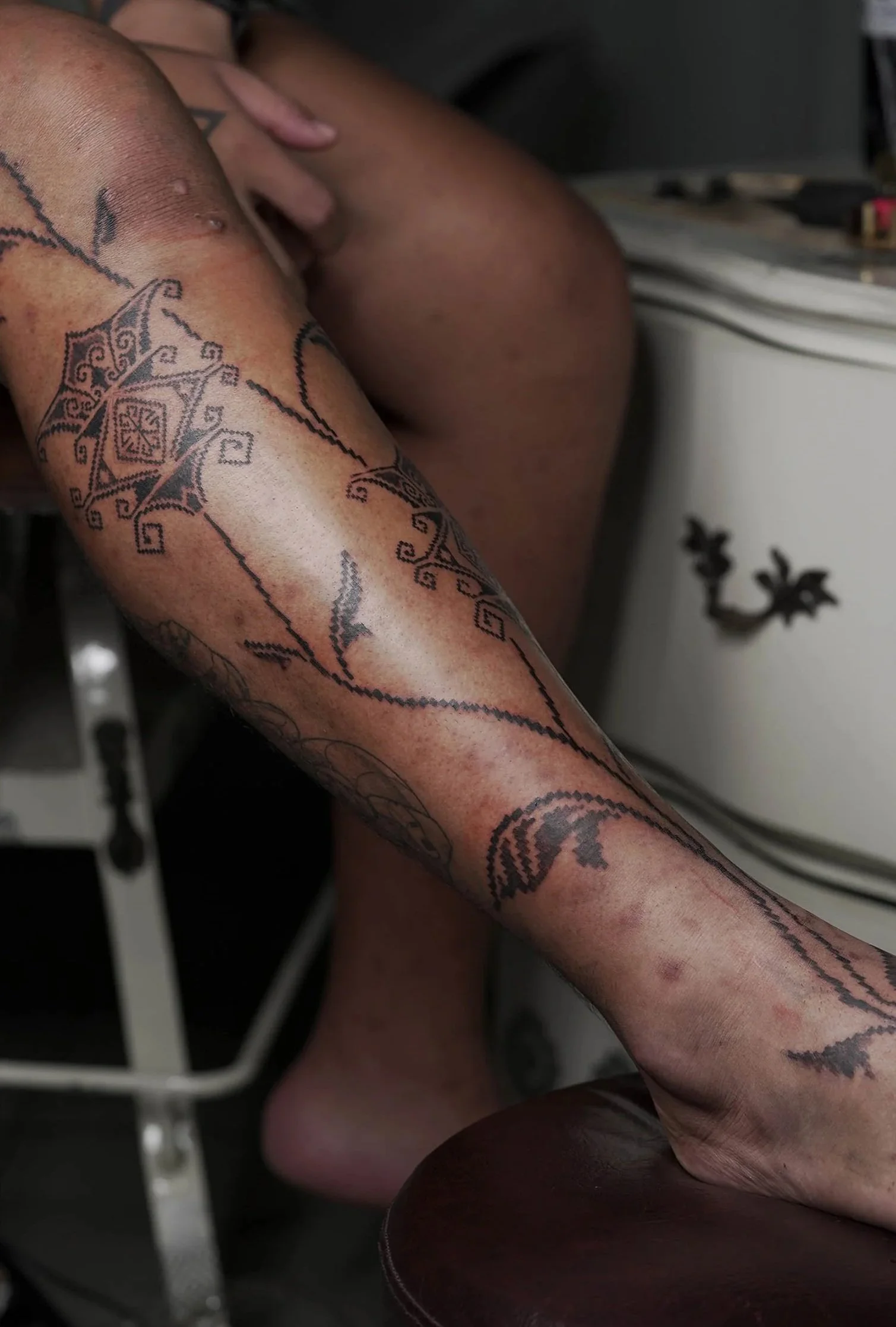 Close-up of a person's leg with a detailed tattoo, resting on their lap.