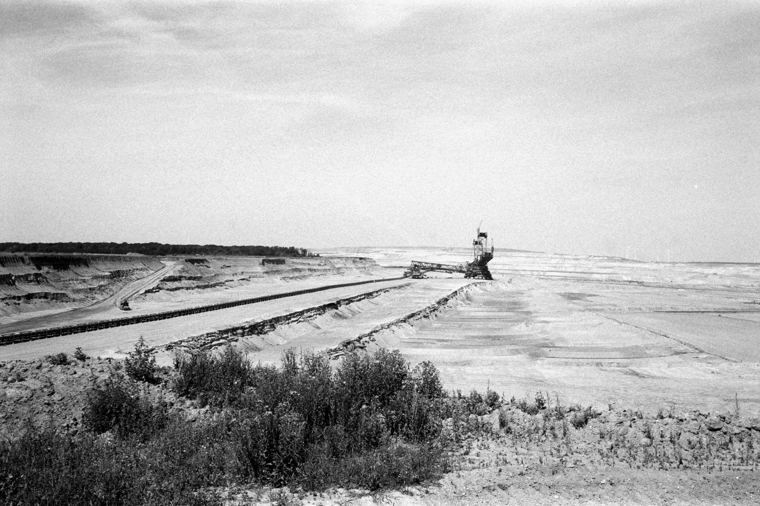 Black and white photograph of an open landscape with a railway construction site, including a large conveyor system and a crane in the distance.