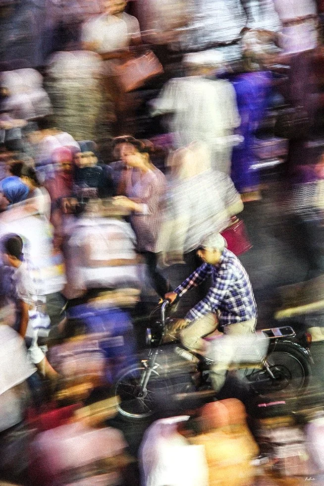 Photographie abstraite — motard au centre, foule en mouvement place Jemaa el-Fna Marrakech, effet de vitesse | Bybadr