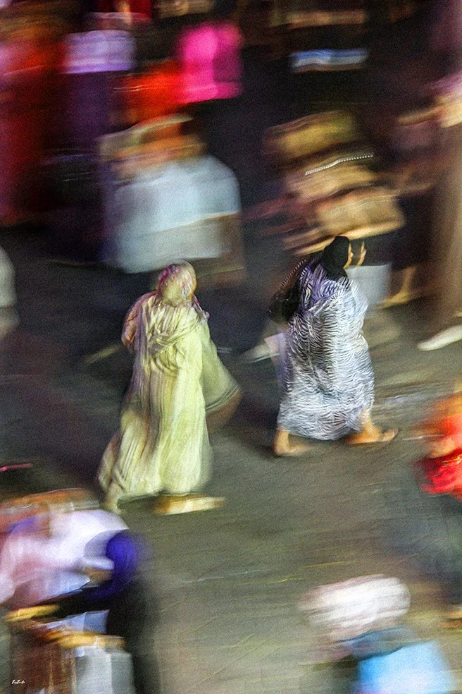 Photographie abstraite — deux femmes en djellaba en mouvement, place Jemaa el-Fna Marrakech la nuit, vue plongeante | Bybadr
