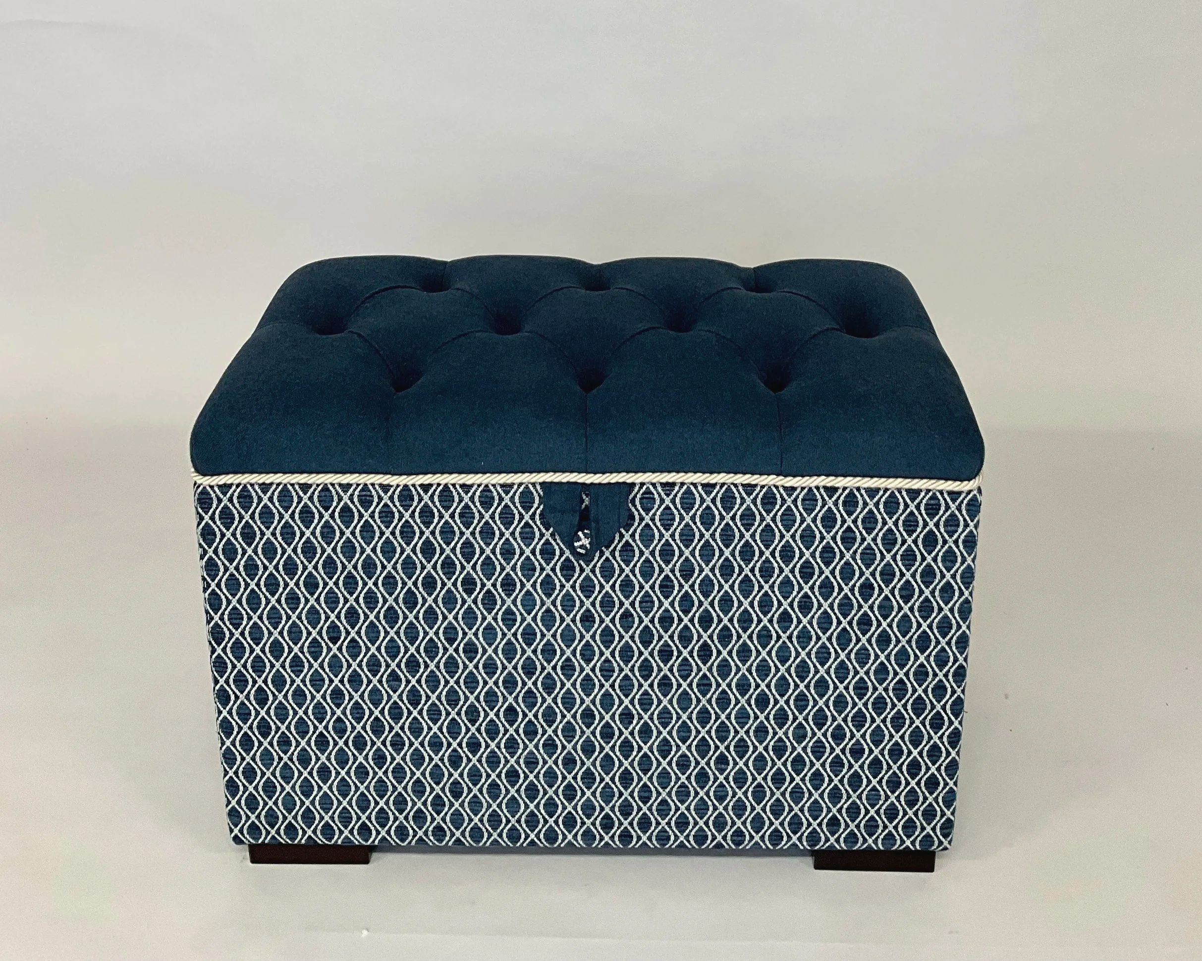 A decorative ottoman with a black tufted top and a black and white patterned bottom, placed against a plain white wall.