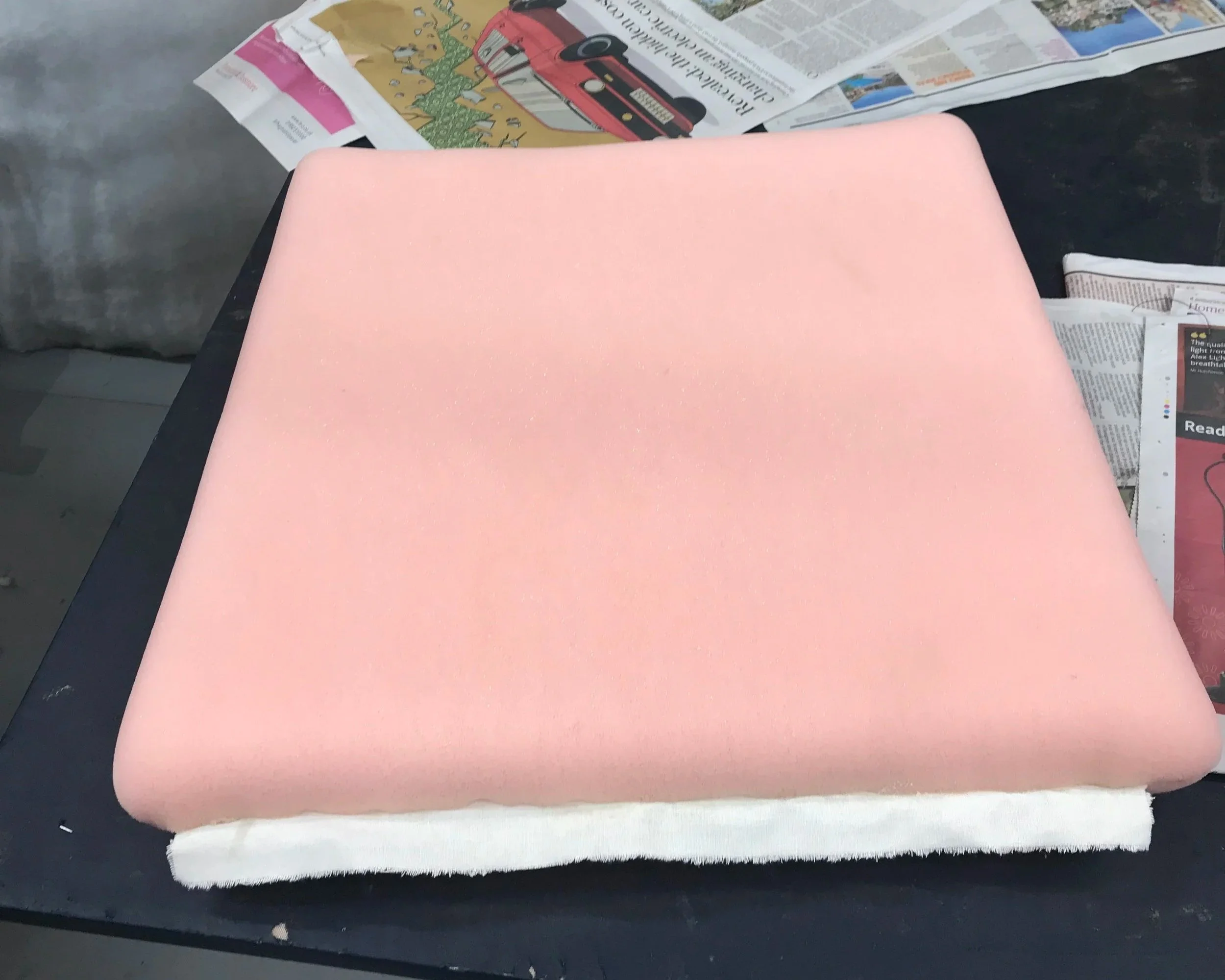 A large piece of light pink foam sits on a white napkin on a black surface, with newspapers in the background.