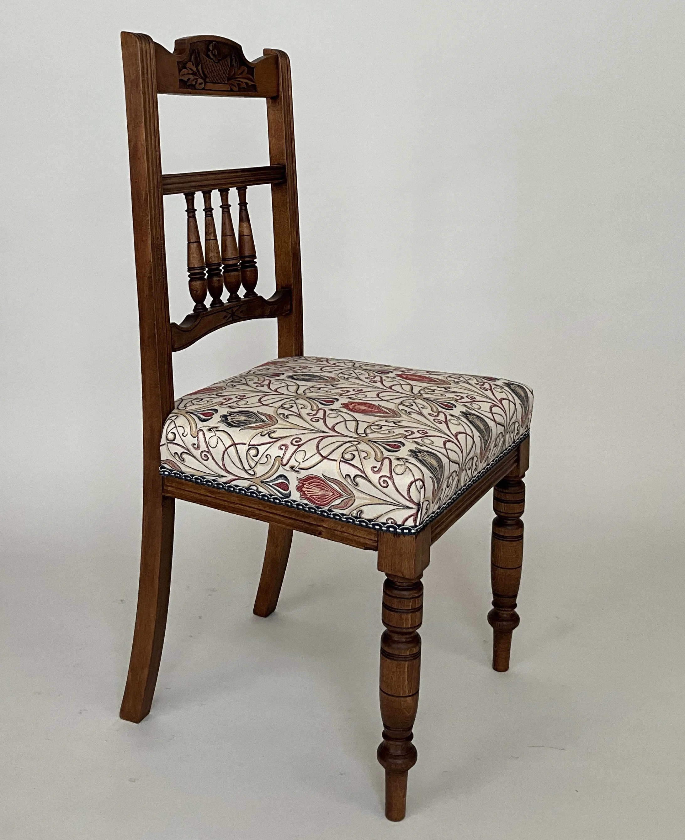 A wooden chair with a decorative carved backrest and a cushioned seat with a floral pattern